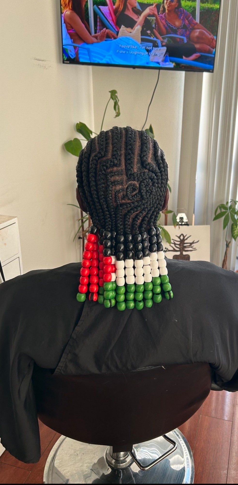 uncredited photo found on tumblr: a person of african descent sits in a stylist's chair and has their hair braided in cornrows and ornated with large red, black, white, and green beads that form the pattern of the Palestinian flag.