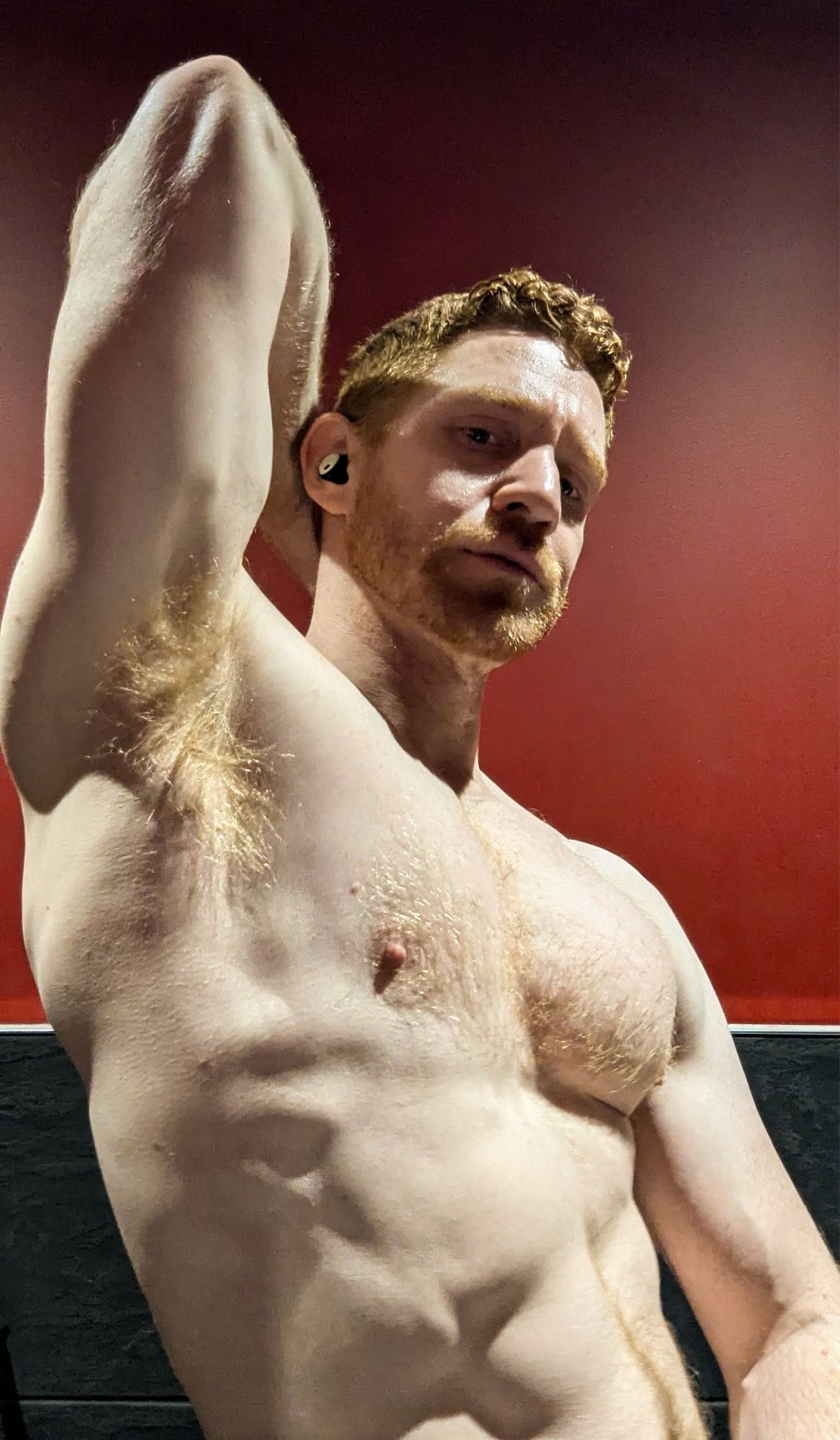 Leander, an athletic redhead, with one arm raised behind his head. His ginger armpit and his large chest area prominent and the light catches his golden body hair.