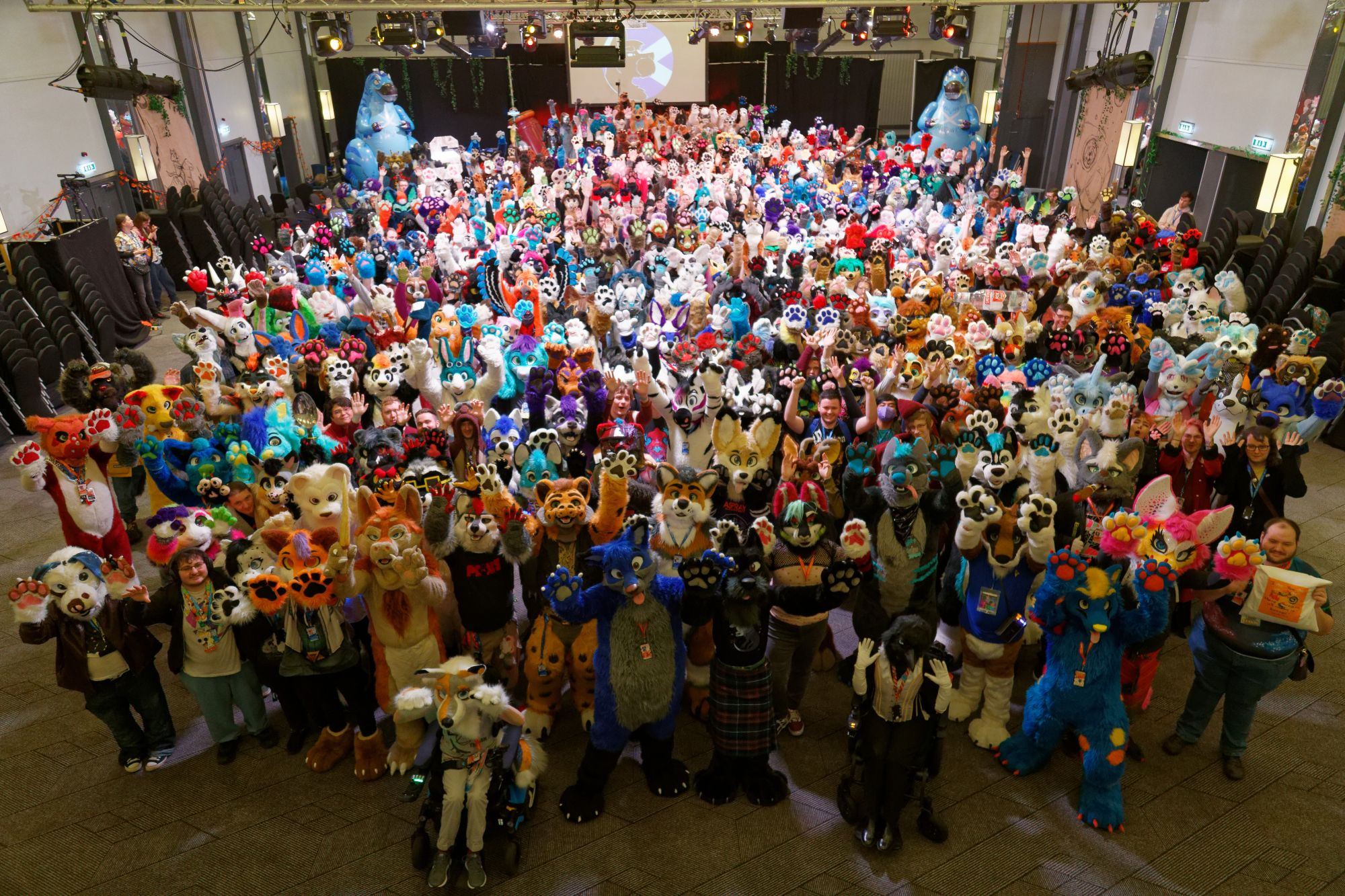 A collection of hundreds of fursuiters and a few other attendees, all holding their paws up at the camera, from the Scotiacon 2024 Group Photo.