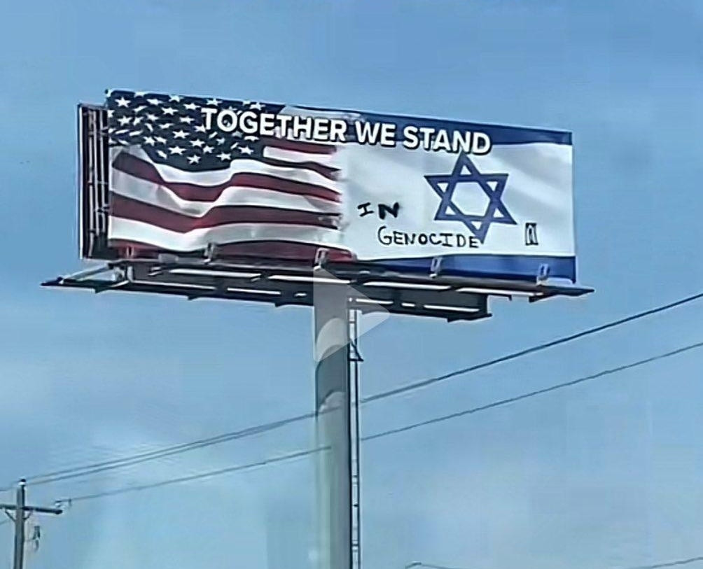 "In genocide" written on a "together we stand billboard featuring a US and Israeli flag