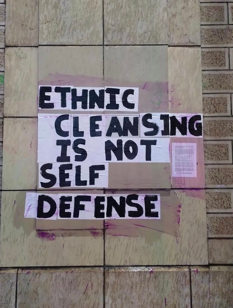 Posters on a wall that spell out "Ethnic cleansing is not self-defense"