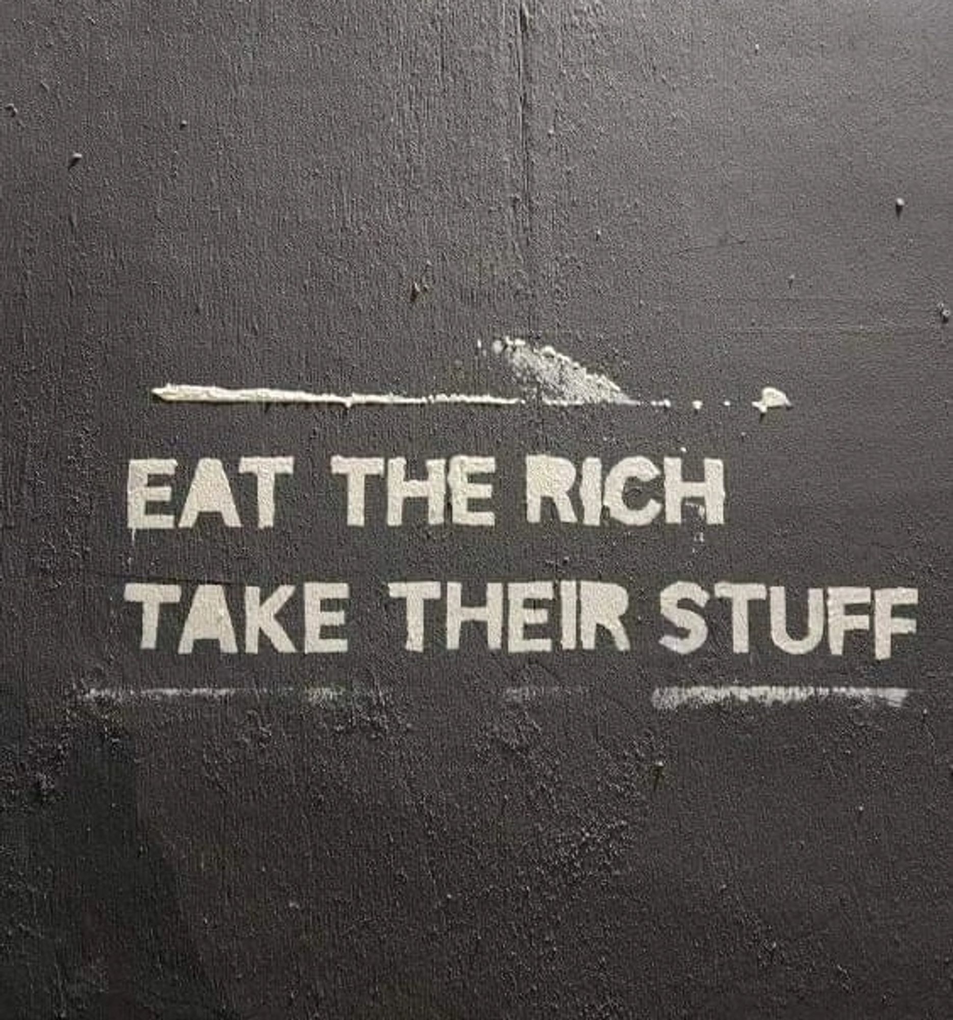 White stencil on a wall that says "Eat the Rich take their stuff"