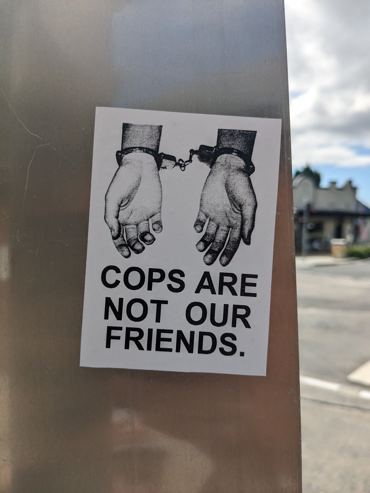 Sticker on a street sign featuring handcuffed hands and the words "Cops are not our friends"