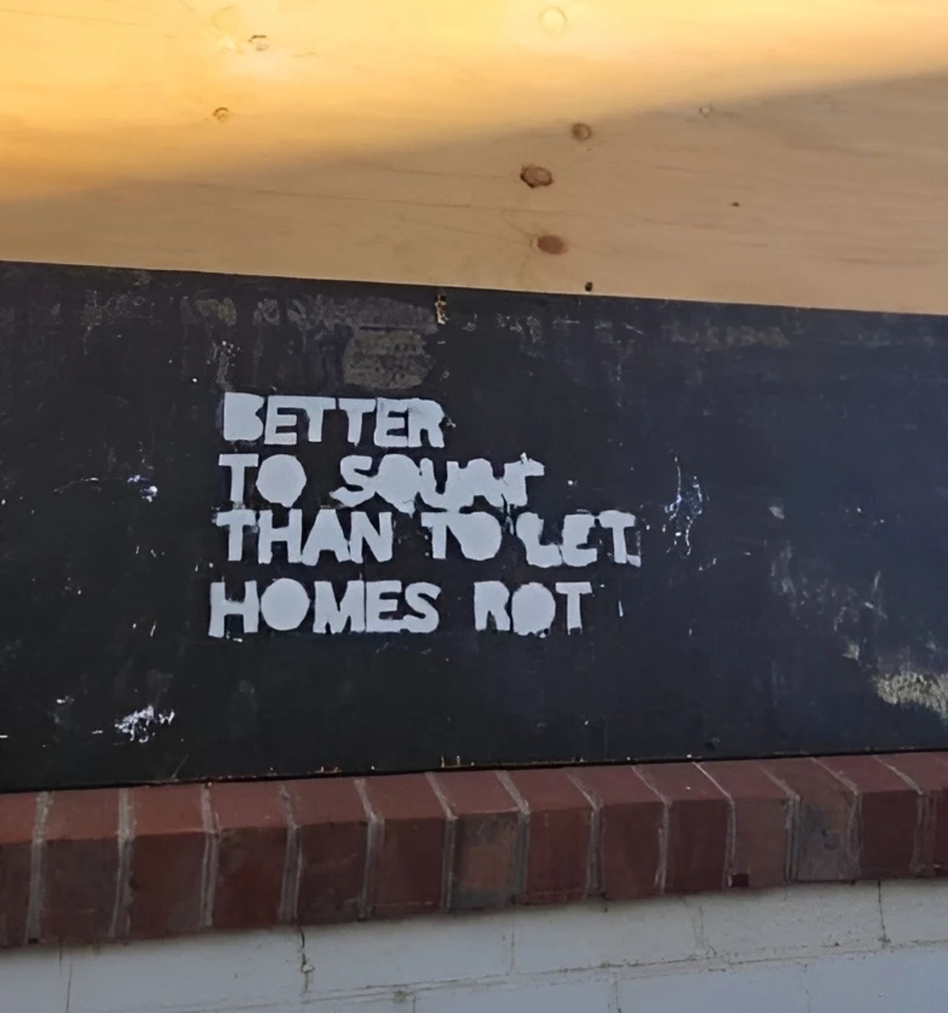 Stencil on a wall that says "Better to Squat than let Homes Rot"