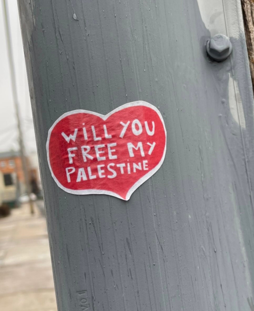 Heart sticker on a pole that says "Will you free my Palestine"