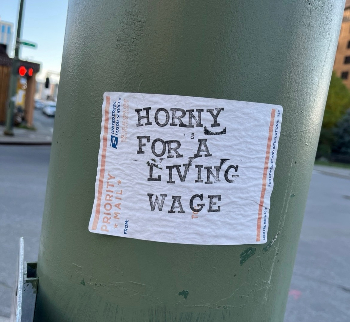 Priority mail sticker on a pole that says "Horny for a living wage"