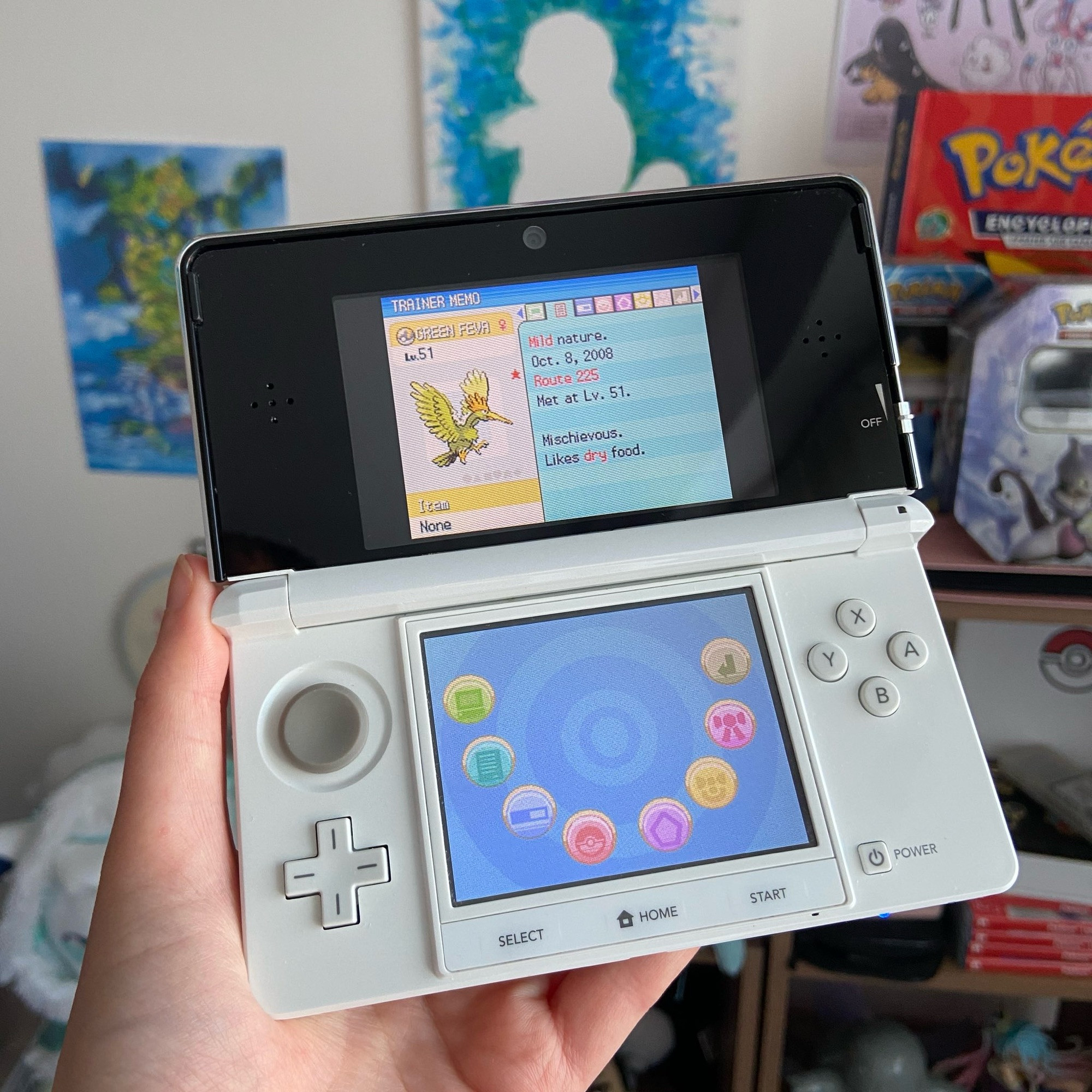 a DS gaming console displaying a shiny Pokémon (a bird that is coloured green/gold)