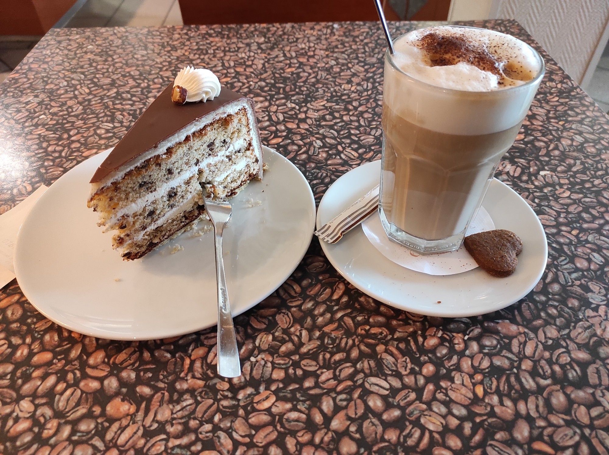 Ein Stück Torte mit Nussbisquit und Vanillecreme und ein Latte Macchiato