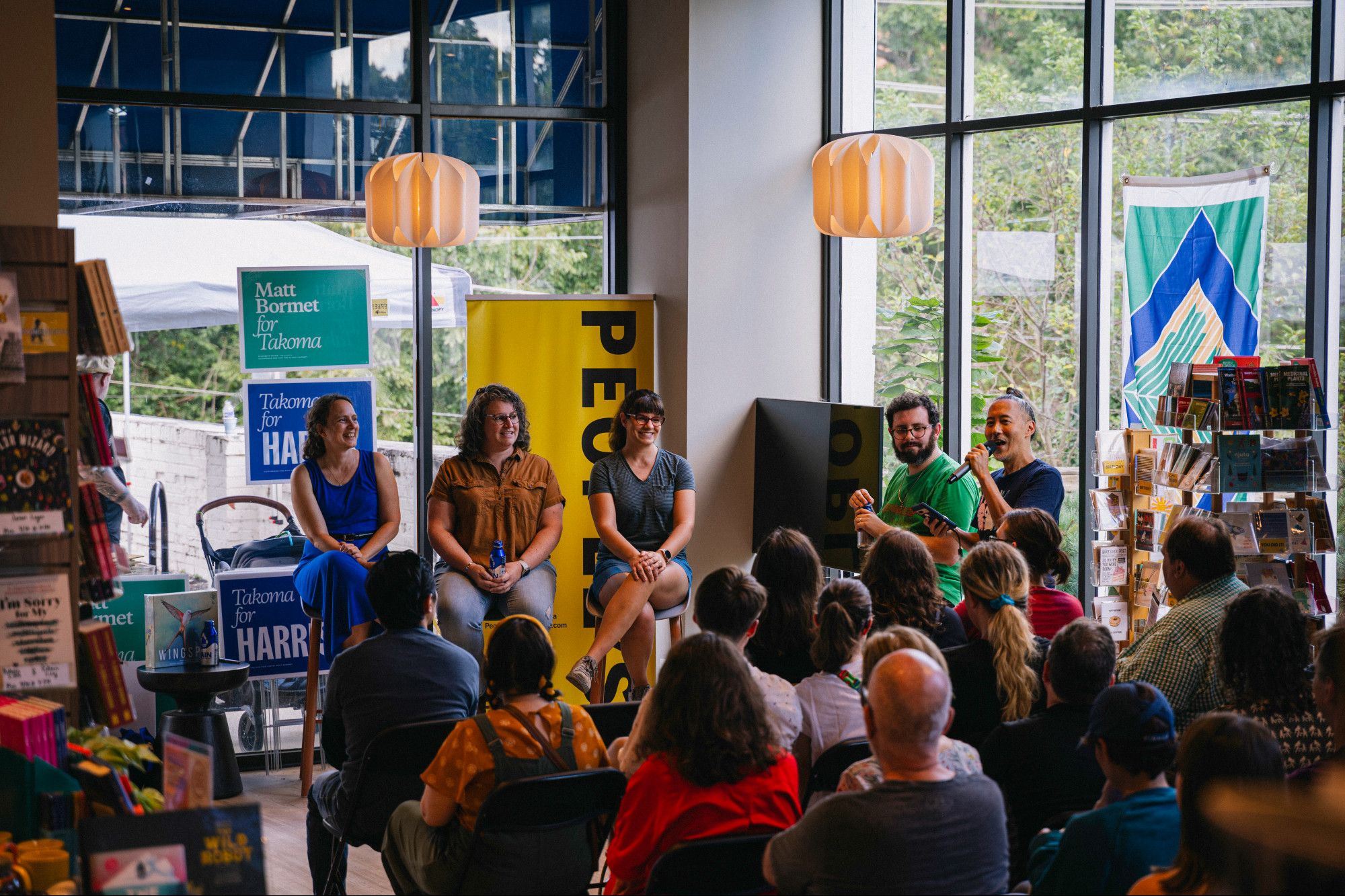 Game designers Elizabeth Hargrave, Tory Brown, Connie Vogelmann, and Alexi Sargeant sitting on tall chairs in front of a seated audience, inside People's Book. Gene Koo (StickyDoodler) is moderating.