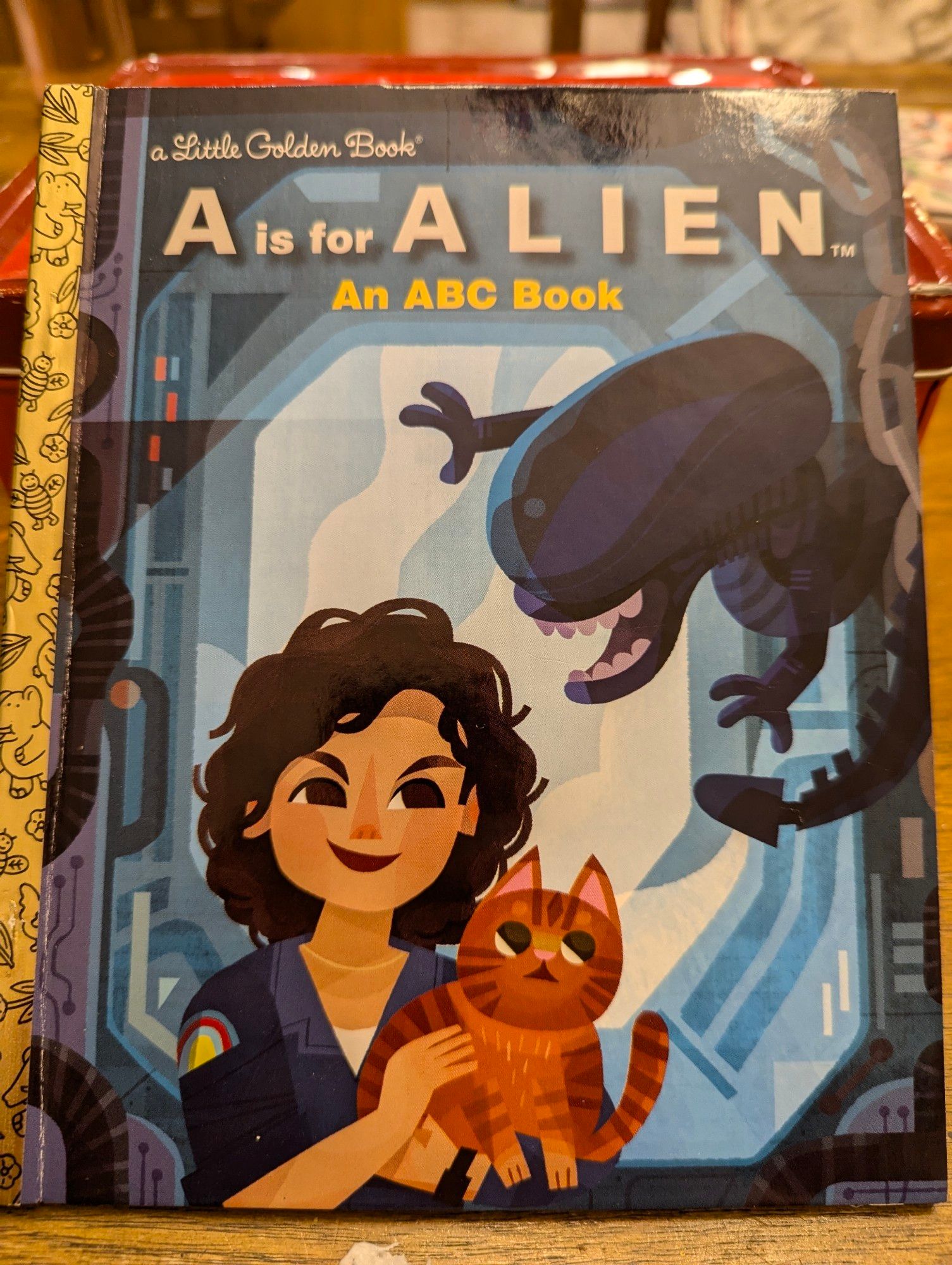 The cover of a Little Golden Book called A is for Alien. Ripley, Jonesy, and a Xenomorph are all there in cartoon format.