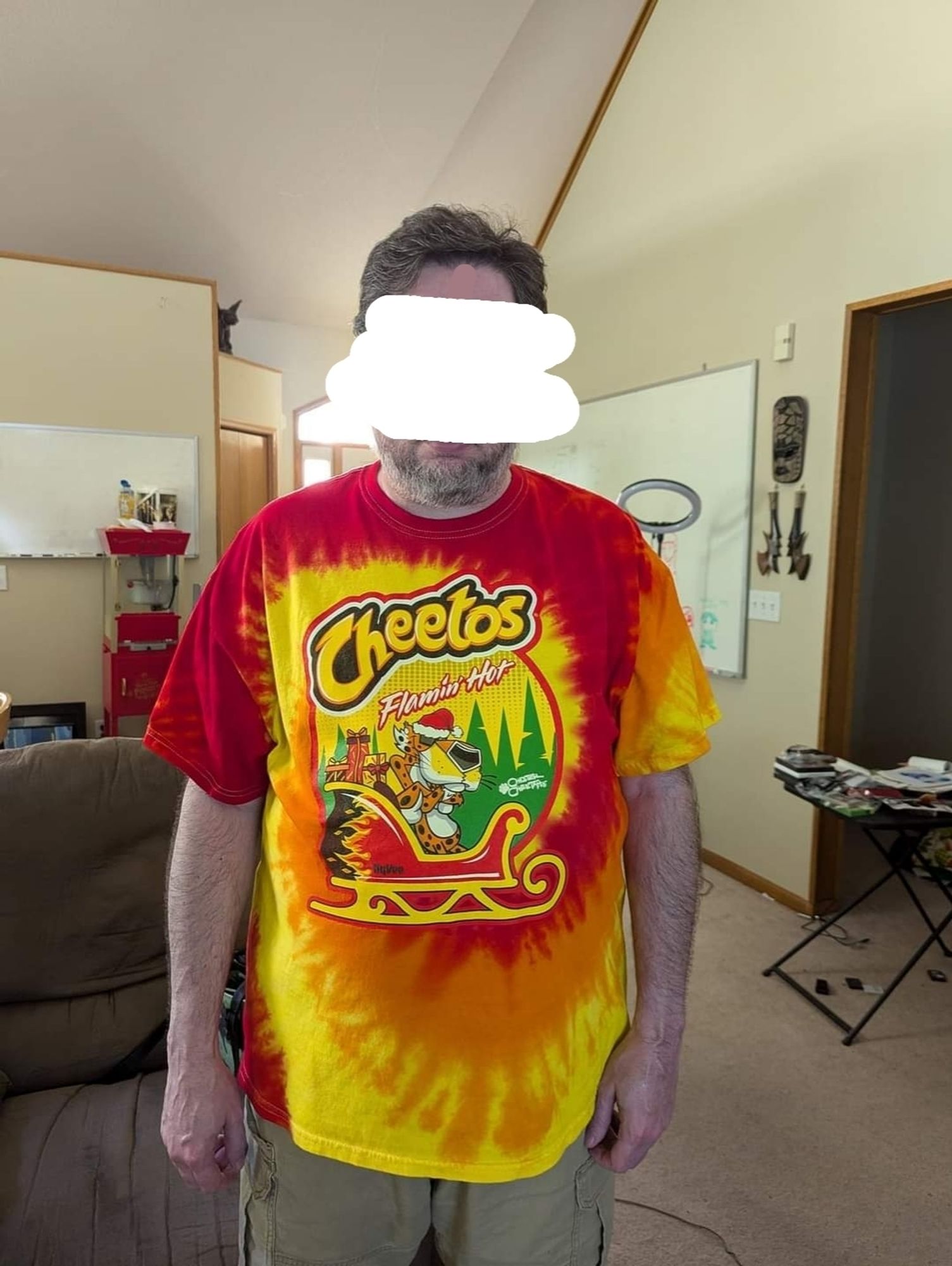 A man wearing a Flamin' Hot Cheetos shirt which is tie-dyed red/orange/yellow and which features Chester Cheetah dressed as Santa, sitting in a sleigh. It's sublime.