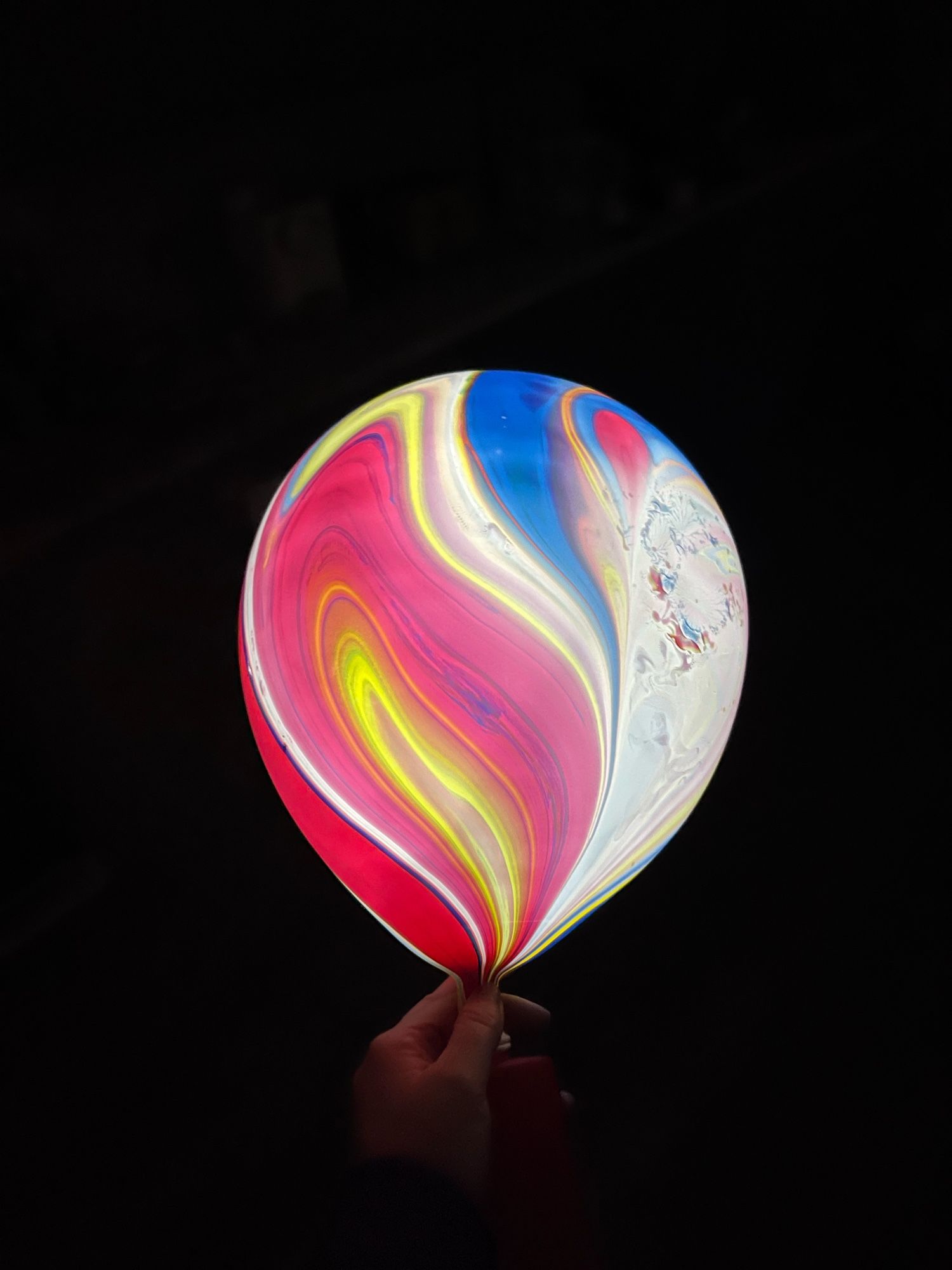 A hand holding a glowing ballon with marble-y patterns against a pitch dark background.