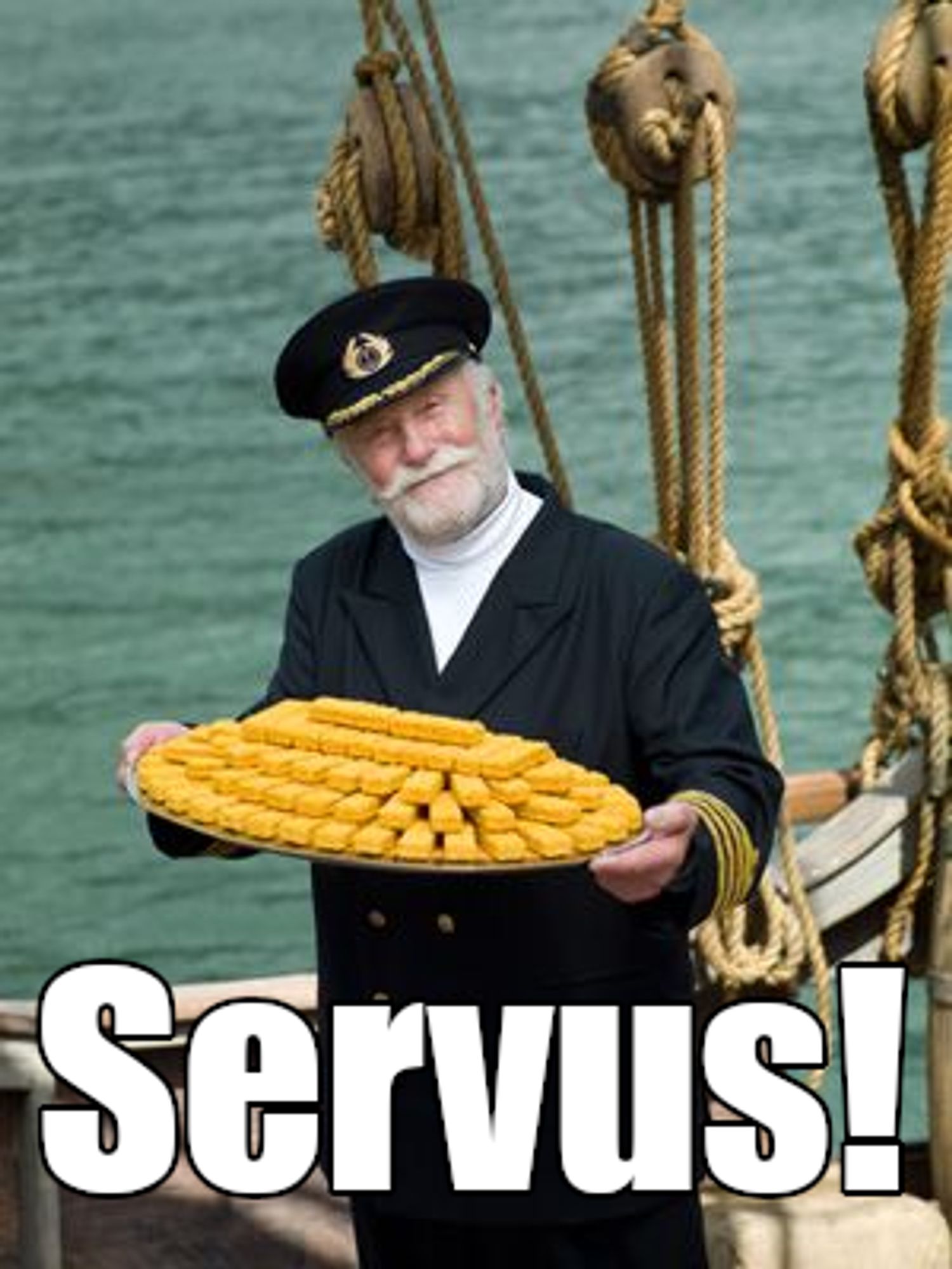 Kapitän Iglo steht auf einem alten Segelschiff, er hält ein Tablett mit vielen Fischstäbchen in den Händen, und lächelt mit geneigtem Kopf in die Kamera. Text 'Servus'