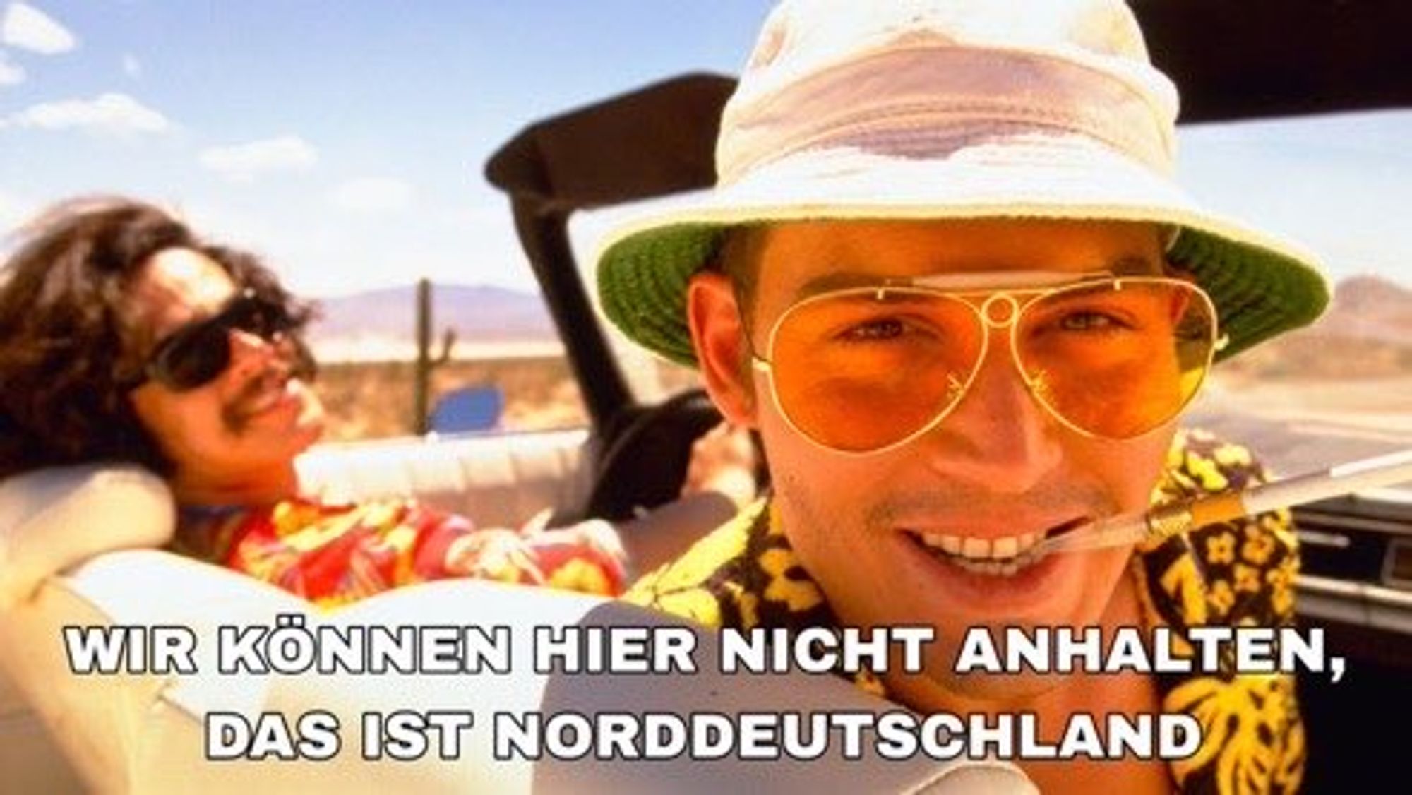 Zu sehen ist eine Szene aus dem Film 'Fear and Loathing in Las Vegas'. Die Beiden Protagonisten sitzen in einem Cabrio und fahren durch die Wüste. Johnny Depp schaut in die Kamera. Text: 'Wir können hier nicht anhalten. Das ist Norddeutschland.'