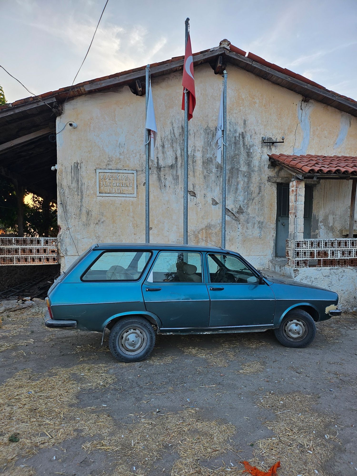 An older Turkish market Renault station wagon, parked in front of the Turkish flag