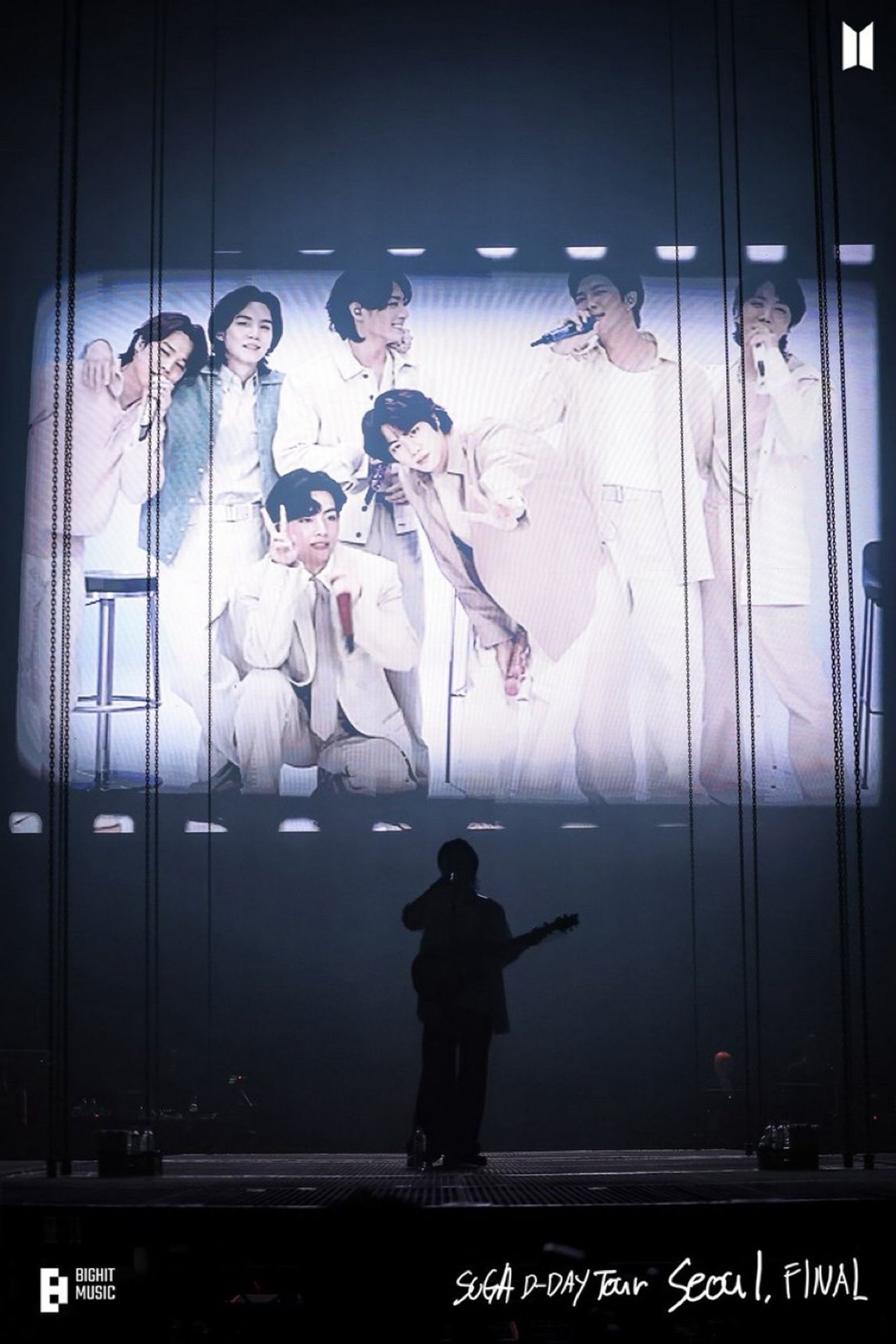 Still from DDay concert by BTS Suga aka AgustD aka Min Yoongi. The picture shows Suga on stage holding a guitar while there is a video montage playing in the background with all the members from Take Two performance