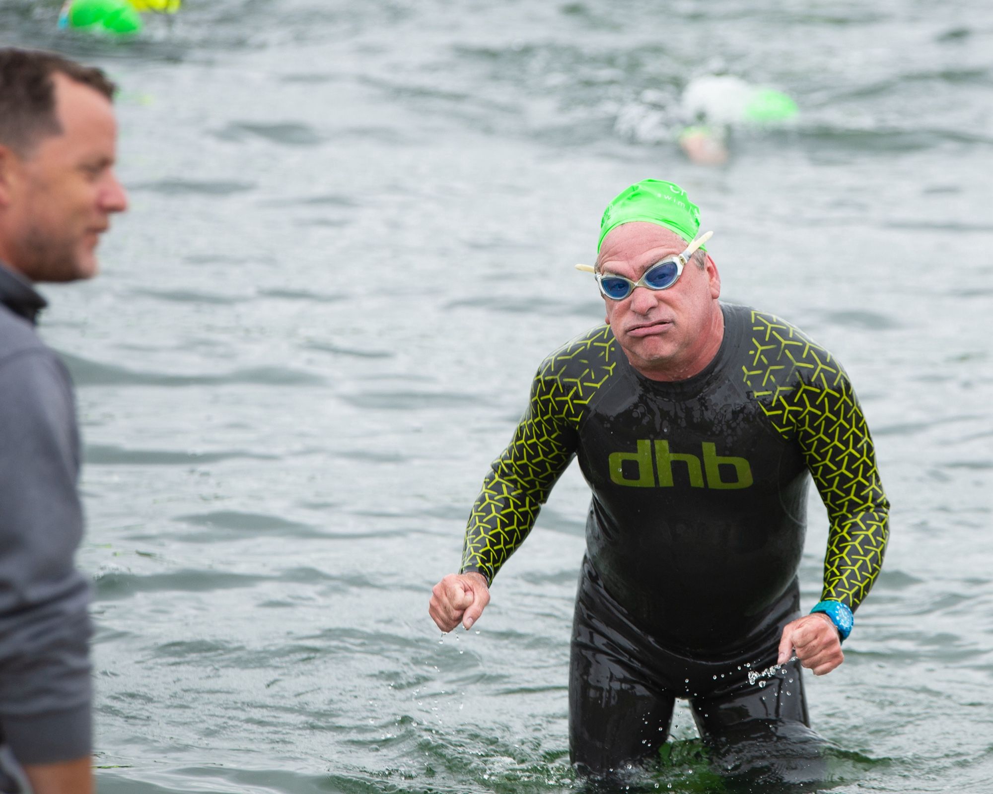 A swimmer walking out of the lake wearing goggles and a weary expression