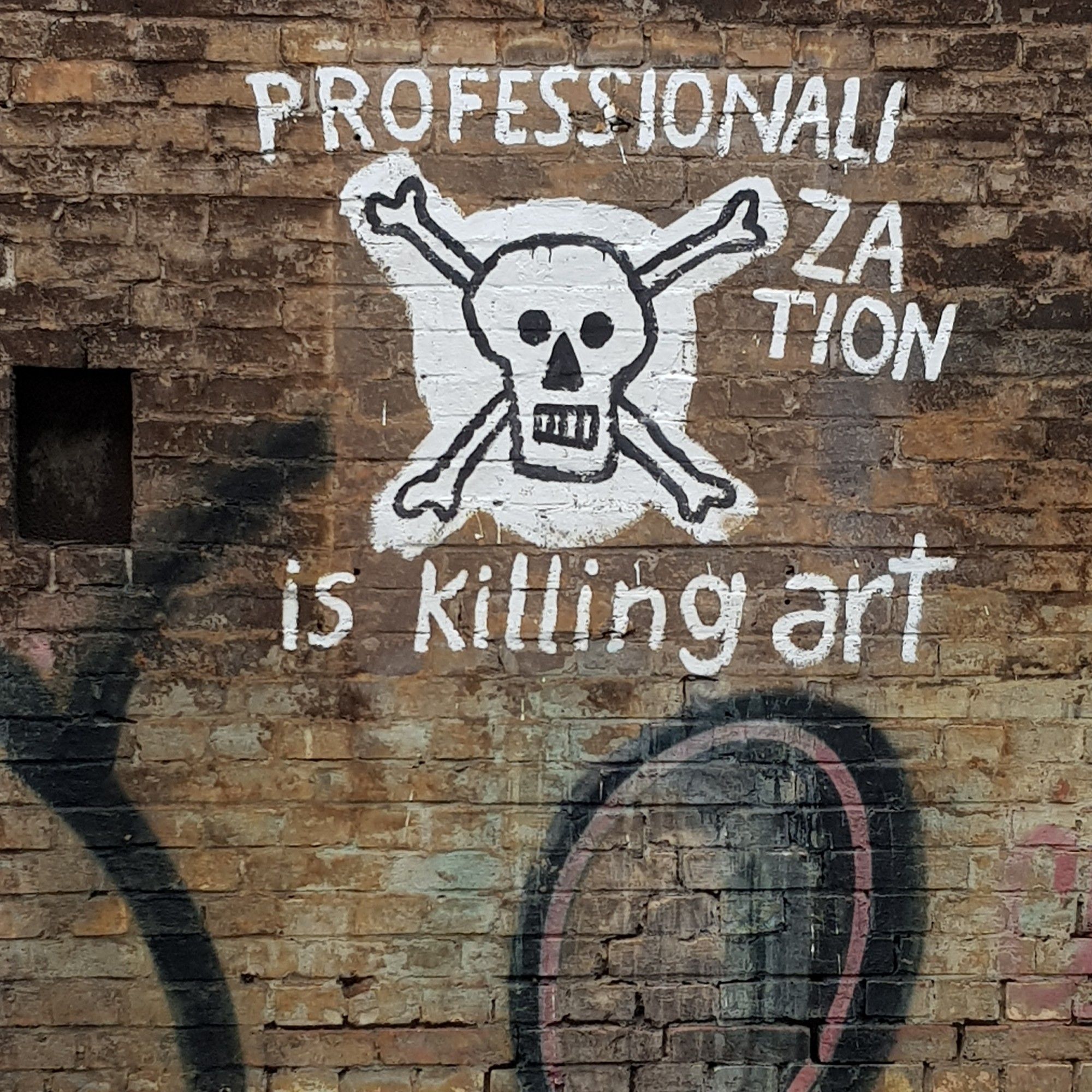 Graffiti auf einer Backsteinwand: ein Totenkopf mit gekreuzten Knochen, begleitet von dem Text 'professionalization is killing art' in weißen Lettern.

Graffiti on a brick wall: a skull and crossbones, accompanied by the text 'professionalization is killing art' in white letters.