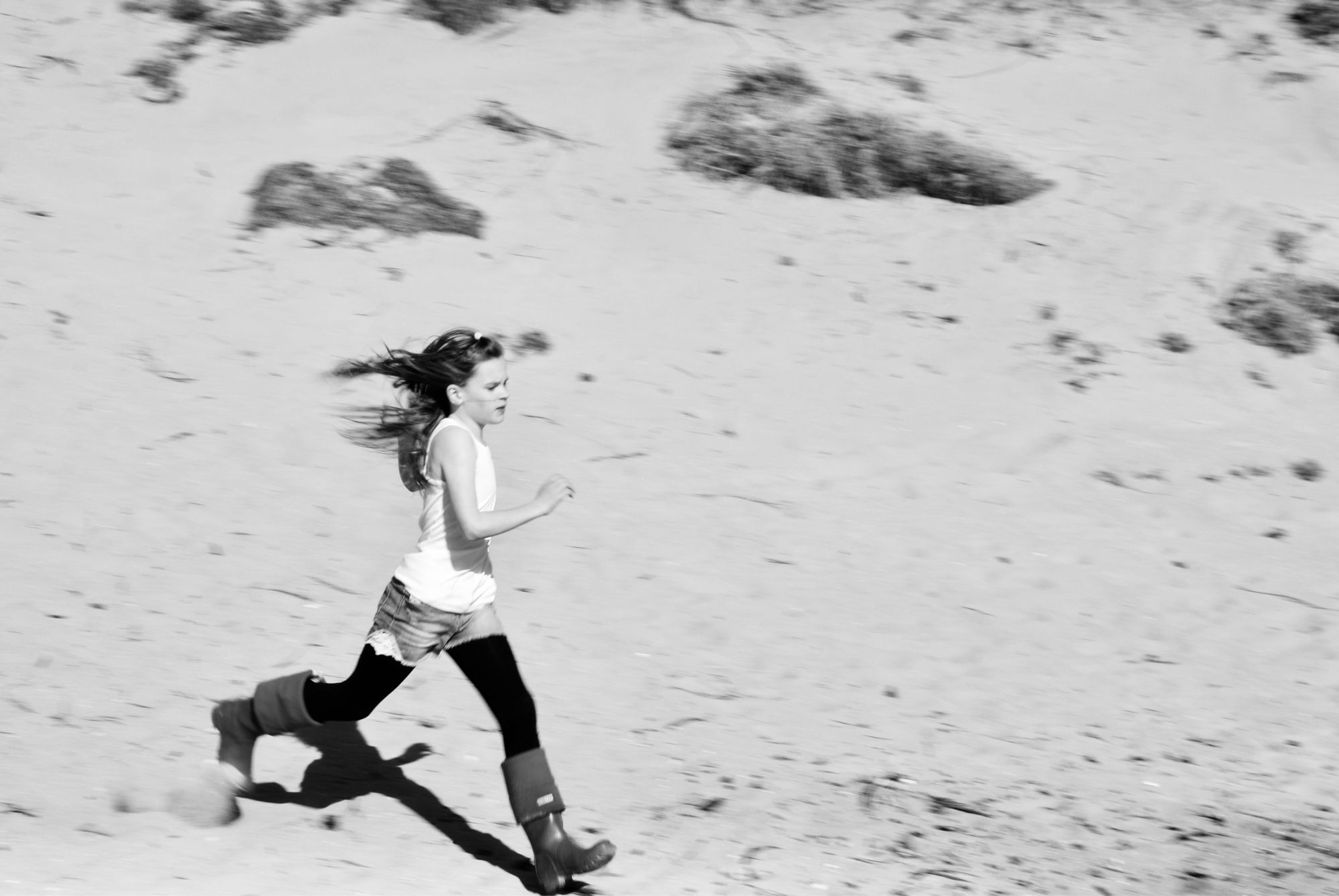 A girl running down a sand dune, her hair is thrown behind her and her face is set in determination