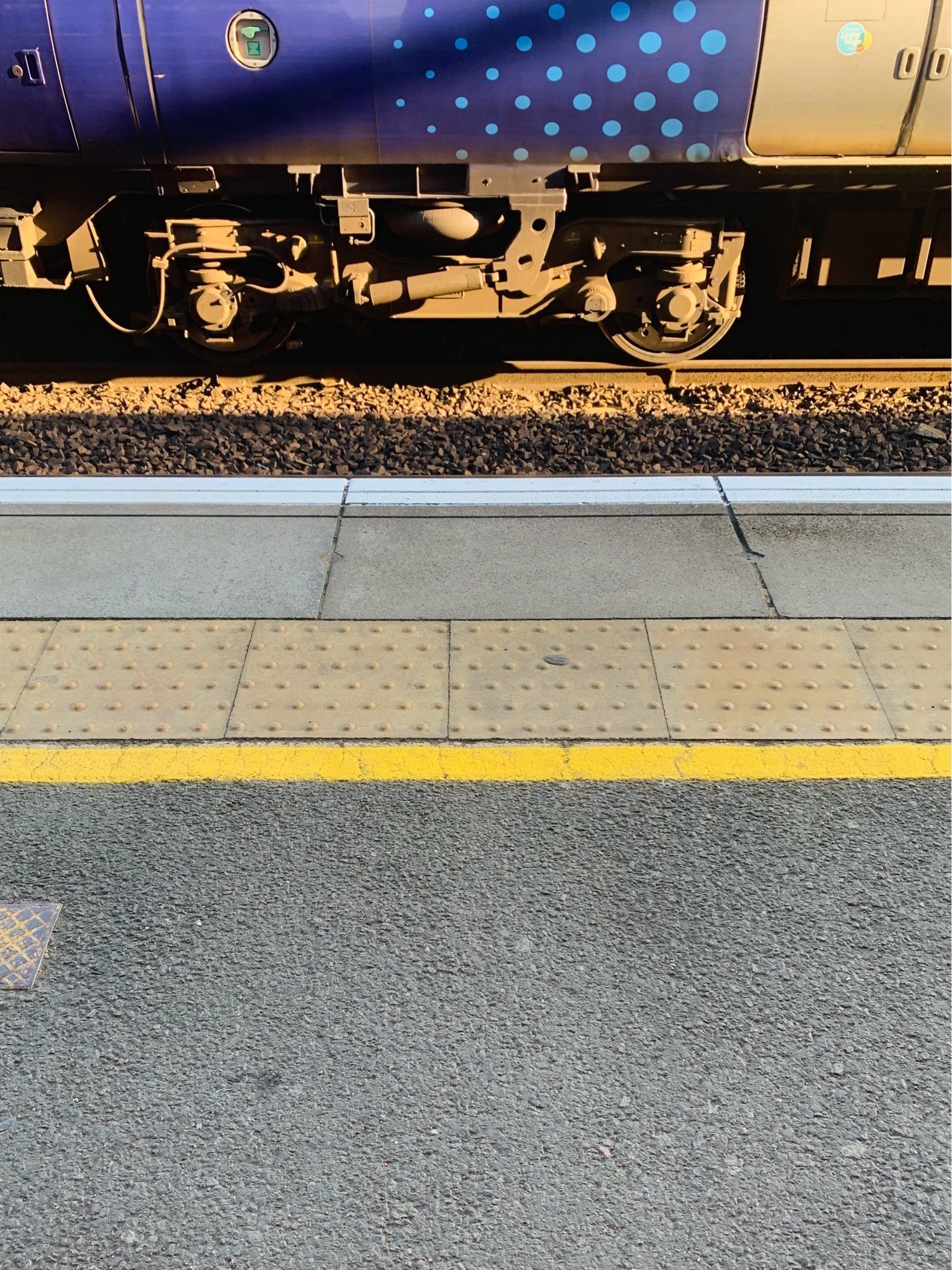 A picture of the platform edge, it has tactile paving for assistance needs and a painted yellow line.  You can see the livery of the bottom of a passing train on the other platform and a little of the track.