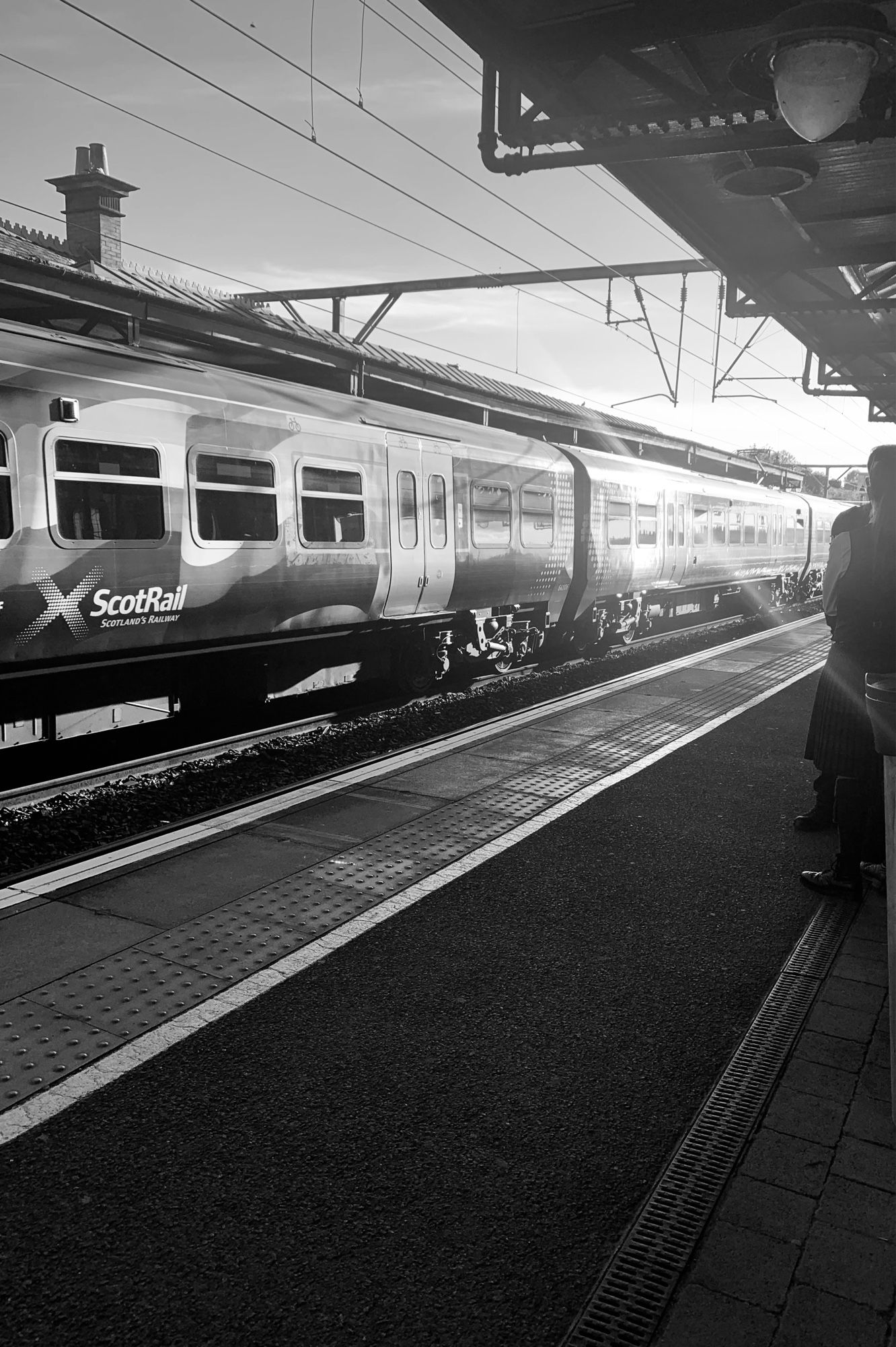 Picture of a train going through the station, it’s in black and white, the sun is bouncing off a carriage.  The shot has strong lines running wide from the left to narrow at the right.