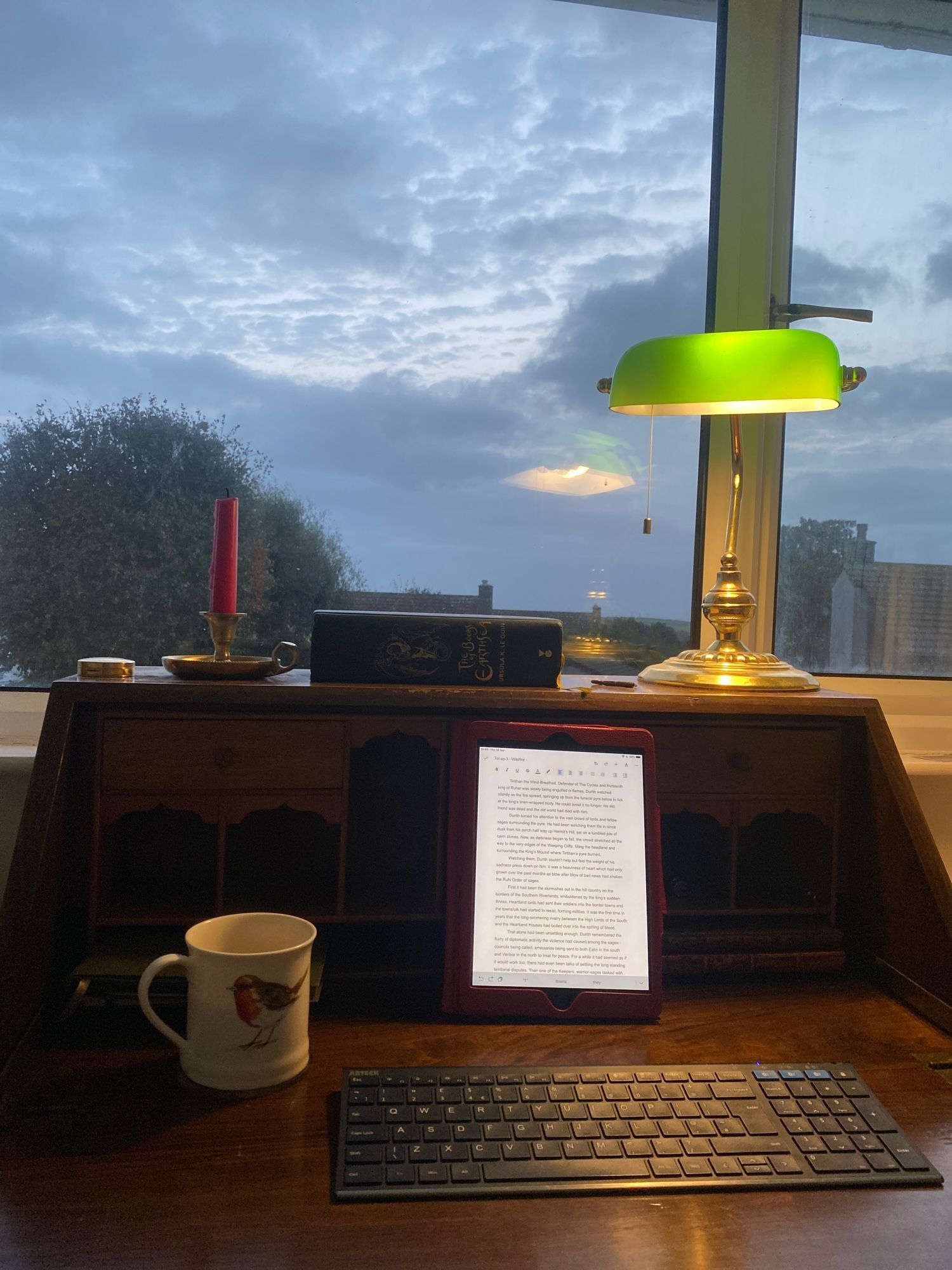 writing desk with coffee, tablet and keyboard, and a sunrise behind.