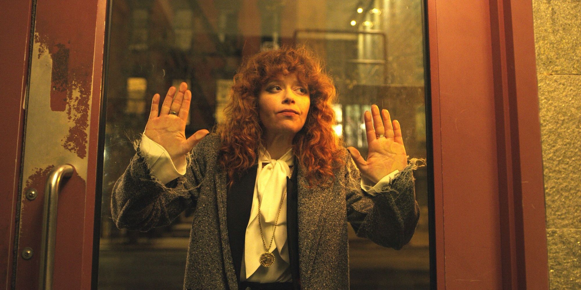 Natasha Lyonne, red curly hair, both hands on a glass door. View from the other side of the door.