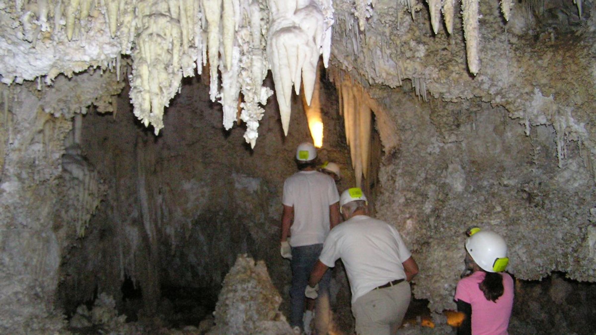 A group of four cavers with hard hats and lights explore an undeveloped cave in New Mexico's Guadalupe Mountains.