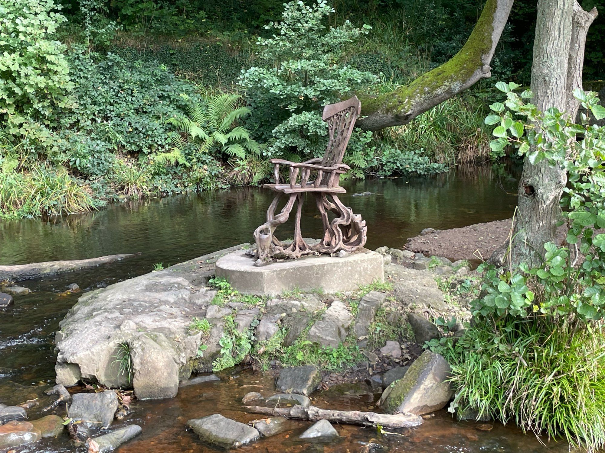 A sculpture of a rocking chair by a river in woodland.