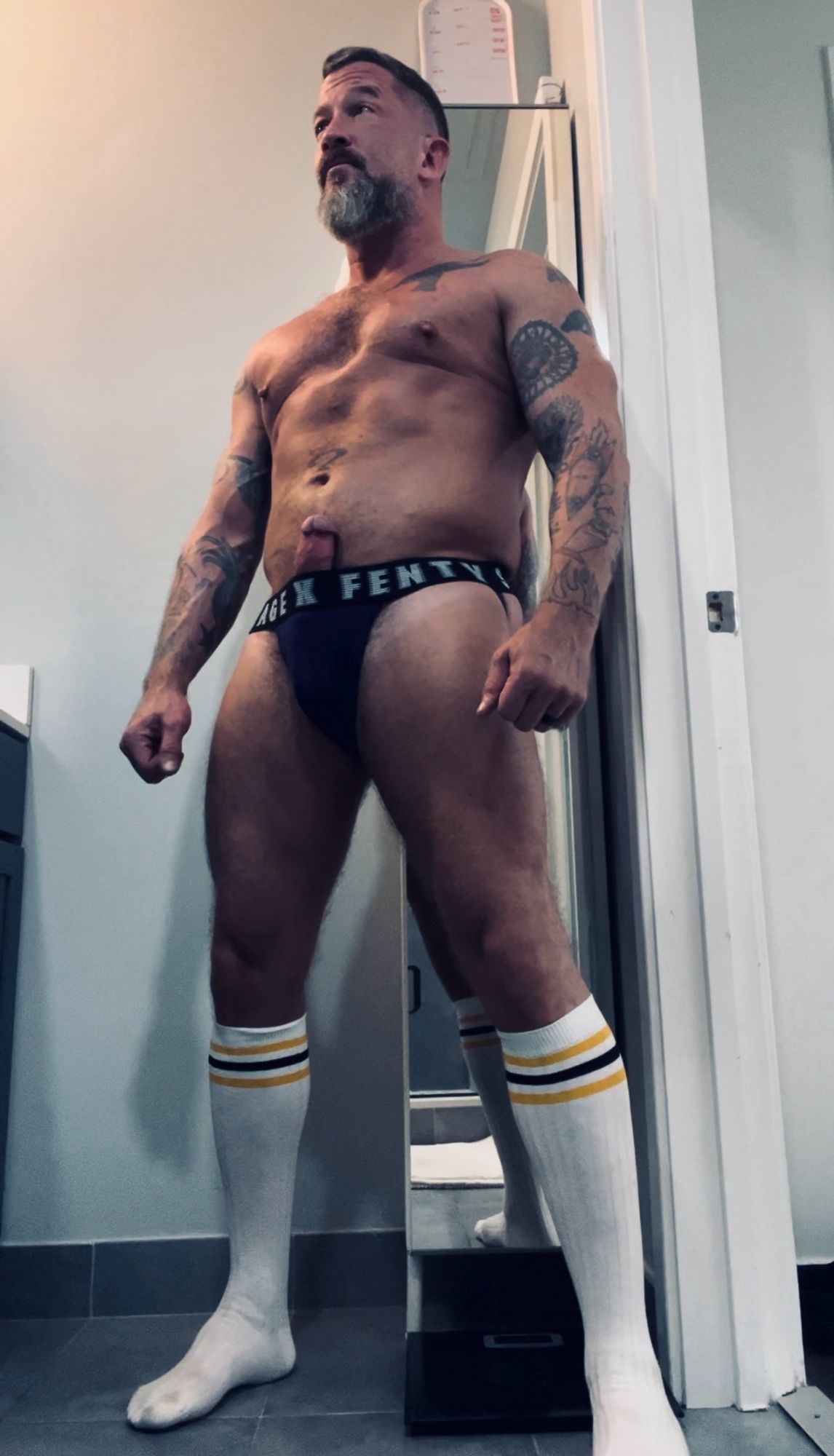 Coach is stripped down to a purple jockstrap and tall white striped socks. His fat erection is poking up through the top of the waistband