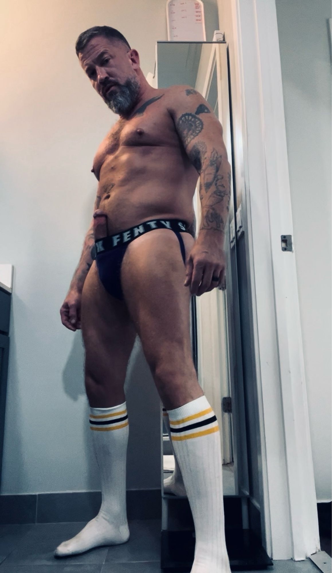 Coach is stripped down to a purple jockstrap and tall white striped socks. His fat erection is poking up through the top of the waistband