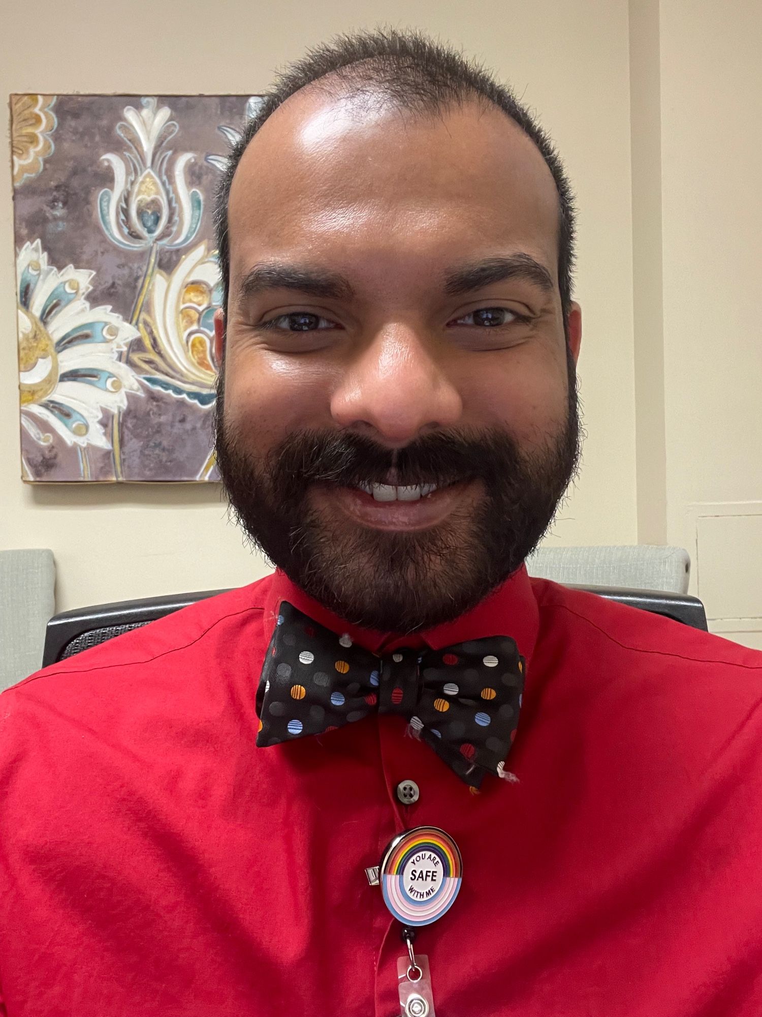 Me, in a bright red dress shirt with black bow tie that has red, blue, and orange polka dots, and a badge reel that says “You Are Safe With Me.”