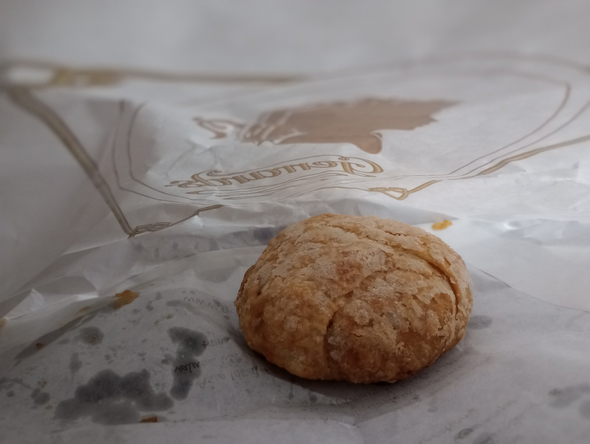 An Eccles cake, photographed in its bag. Note the sheen on the paper. That's not grease. Oh, no. That's from where the caramelised sugar and butter from the pastry  plus from where the raisin filling has bubbled out, giving the cake a butterscotch Maillard underside.