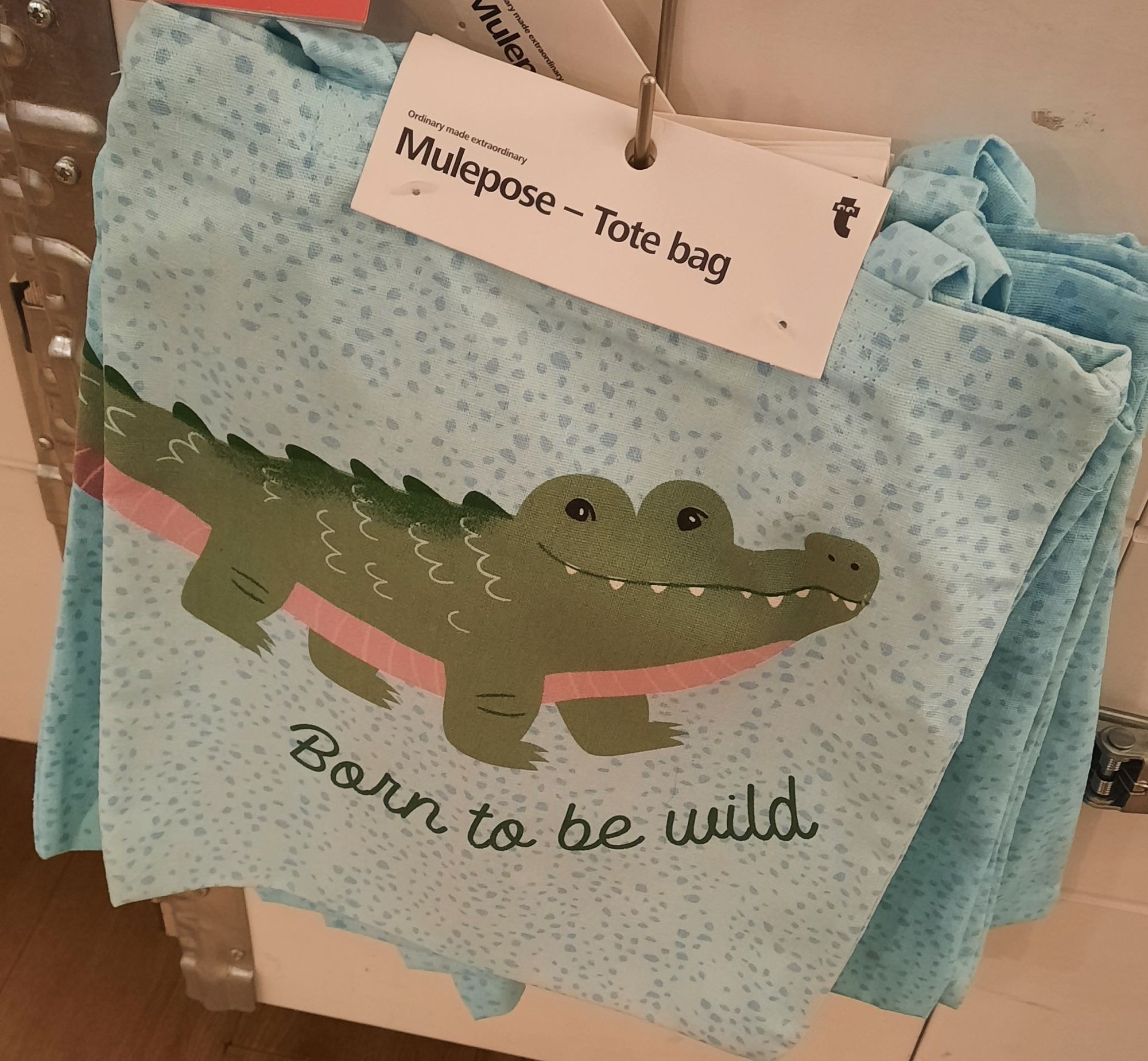 Foto de una tote bag azul con un cocodrilo dibujado sonriendo. Debajo el texto "born to be wild"