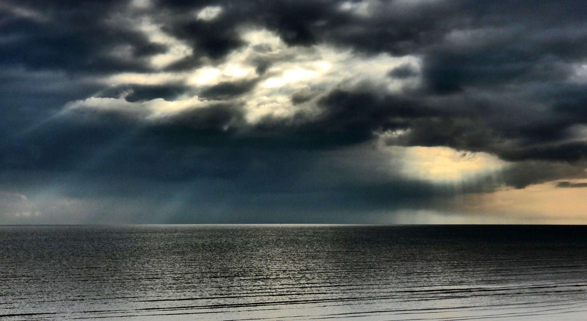 Sunbursts breaking through storm clouds over the sea.