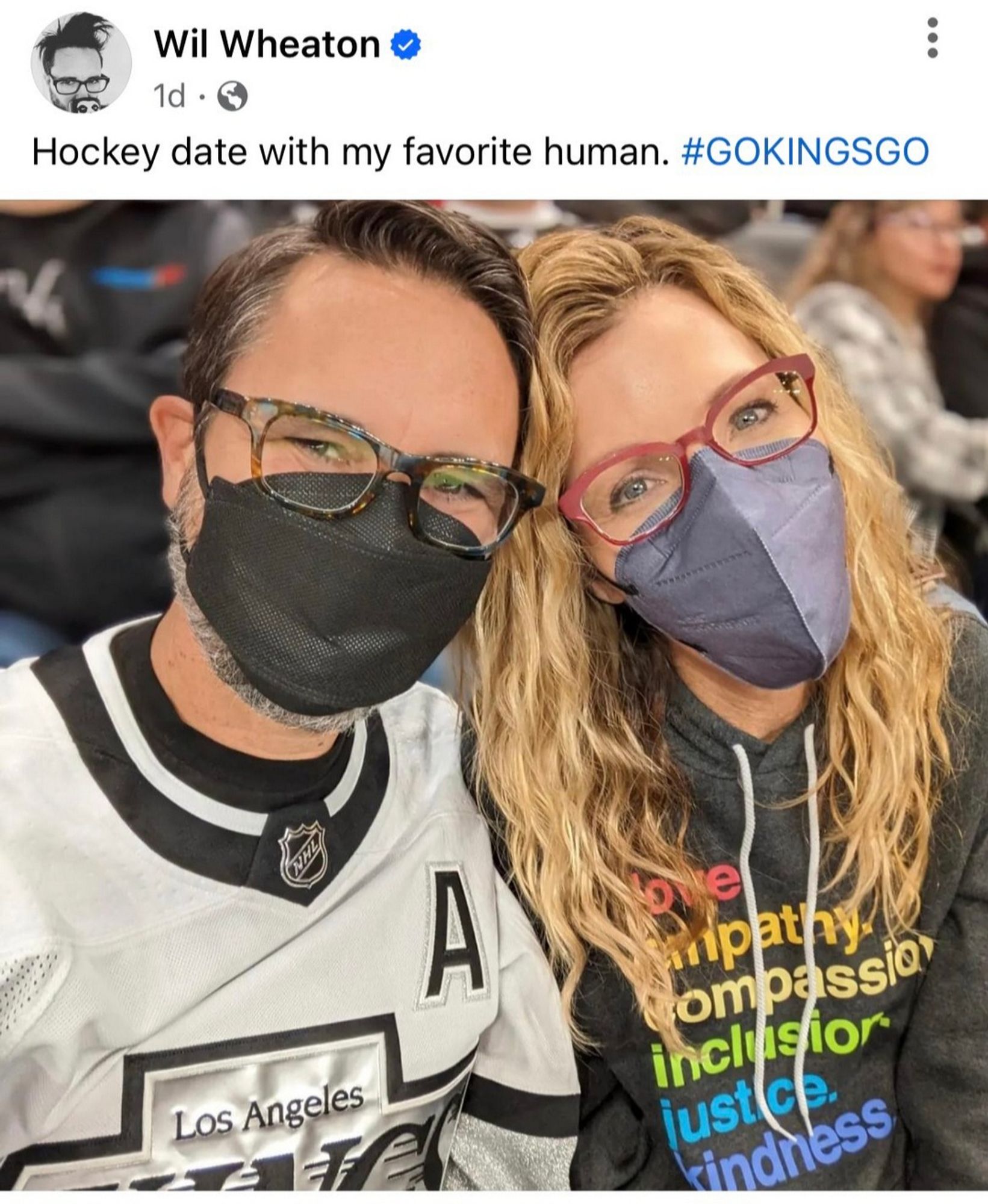 Photo of Wil Wheaton and his wife at a hockey game, both wearing masks.