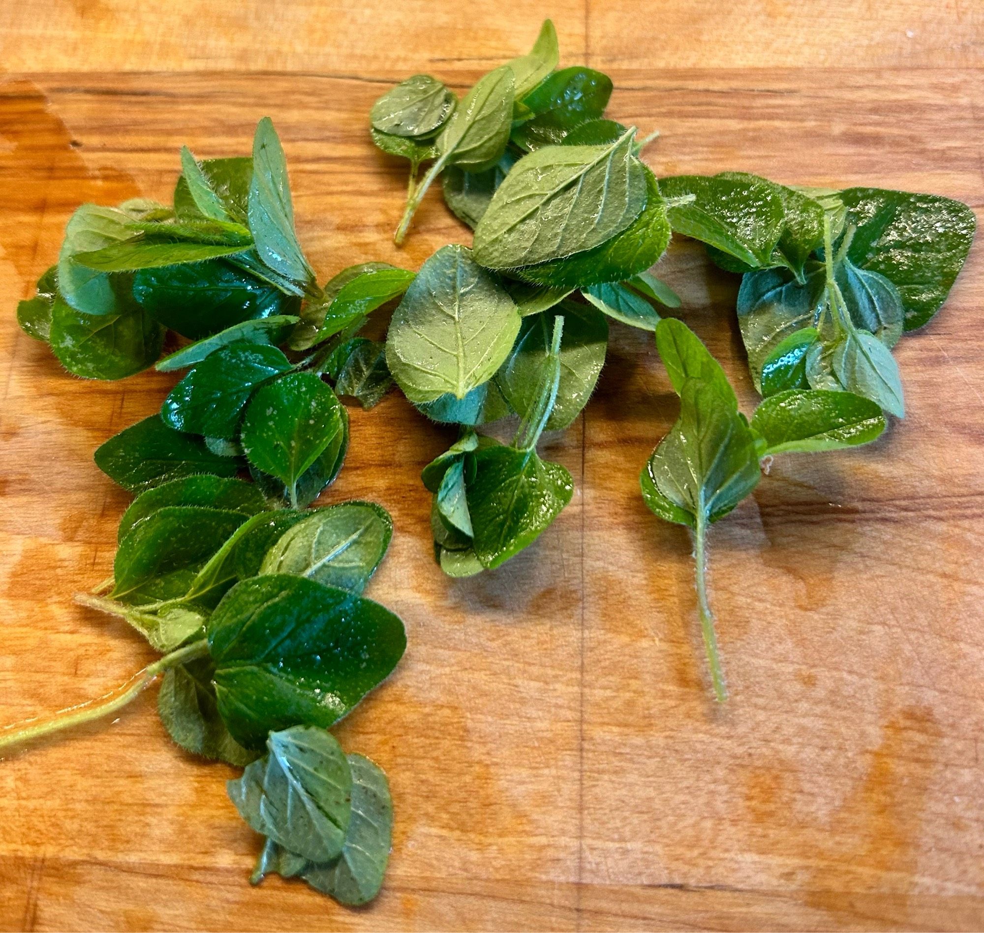 Fresh oregano leaves on a wood cutting board.