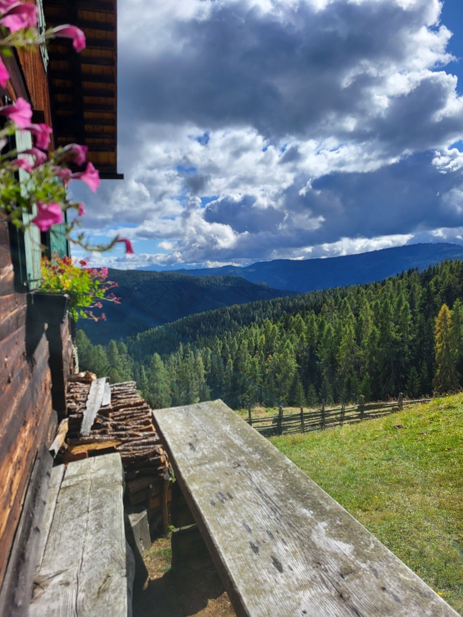 bankerl vor der almhütte mir blick ins tal mig wald und bergen. blauer himmel mit wolken