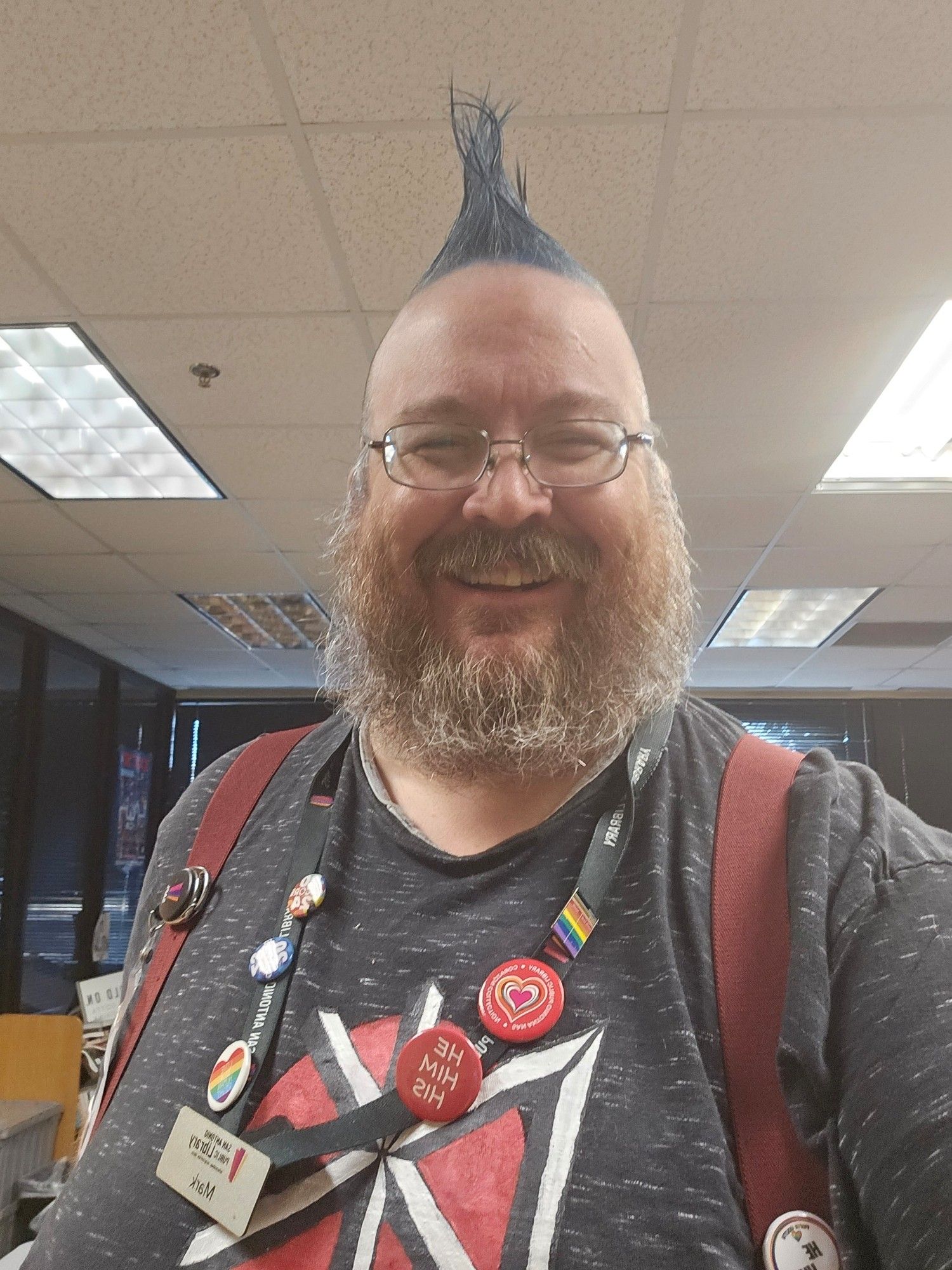 Middle aged white man with brown/grey beard and a blue mohawk, wearing a Dead Kennedys t-shirt and a work name badge.