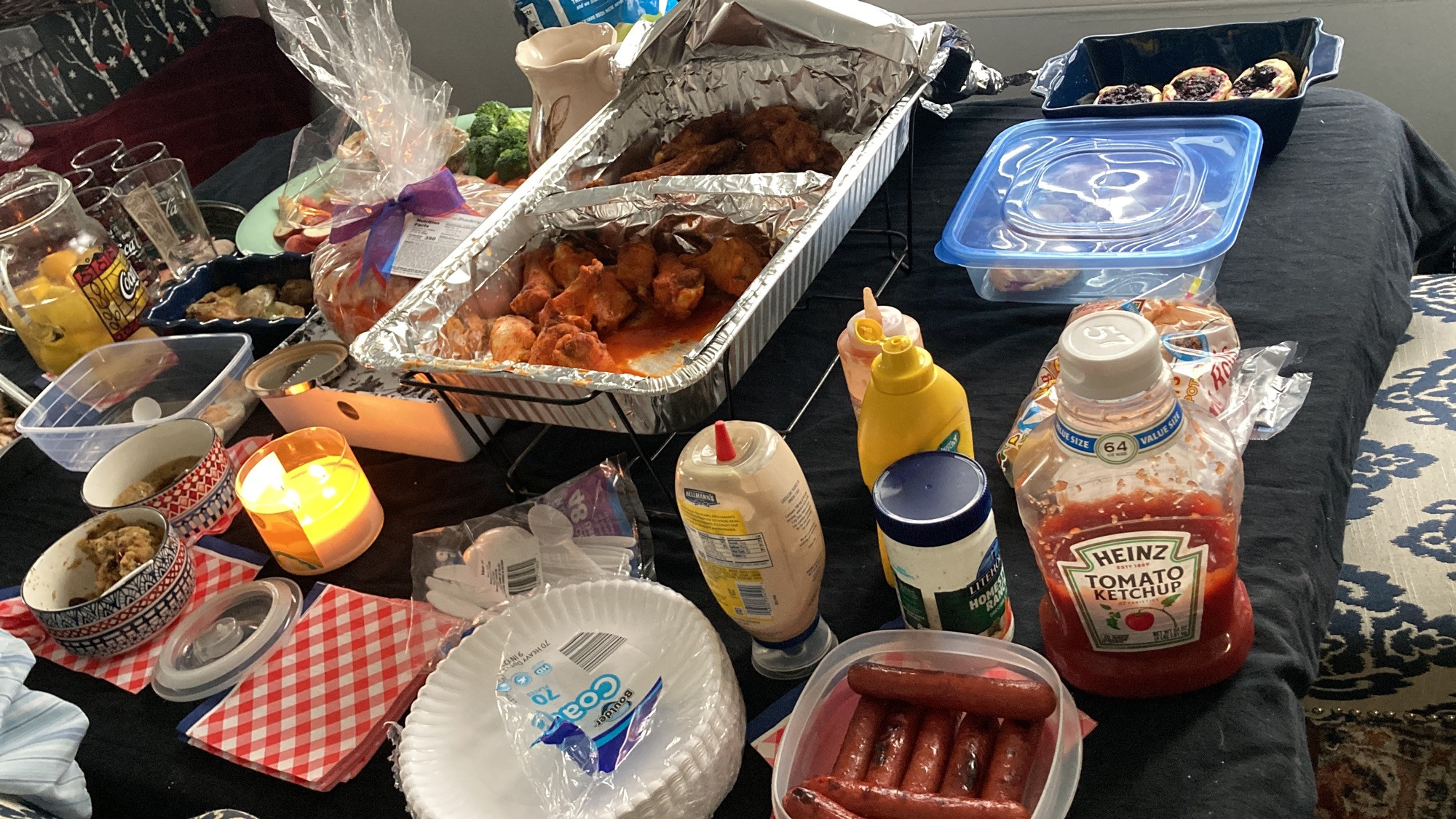 Table full of food, hotdogs, chicken wings (old bay and hot) puff pasties, roasted chicken, potato salad, lemonade, and condiments