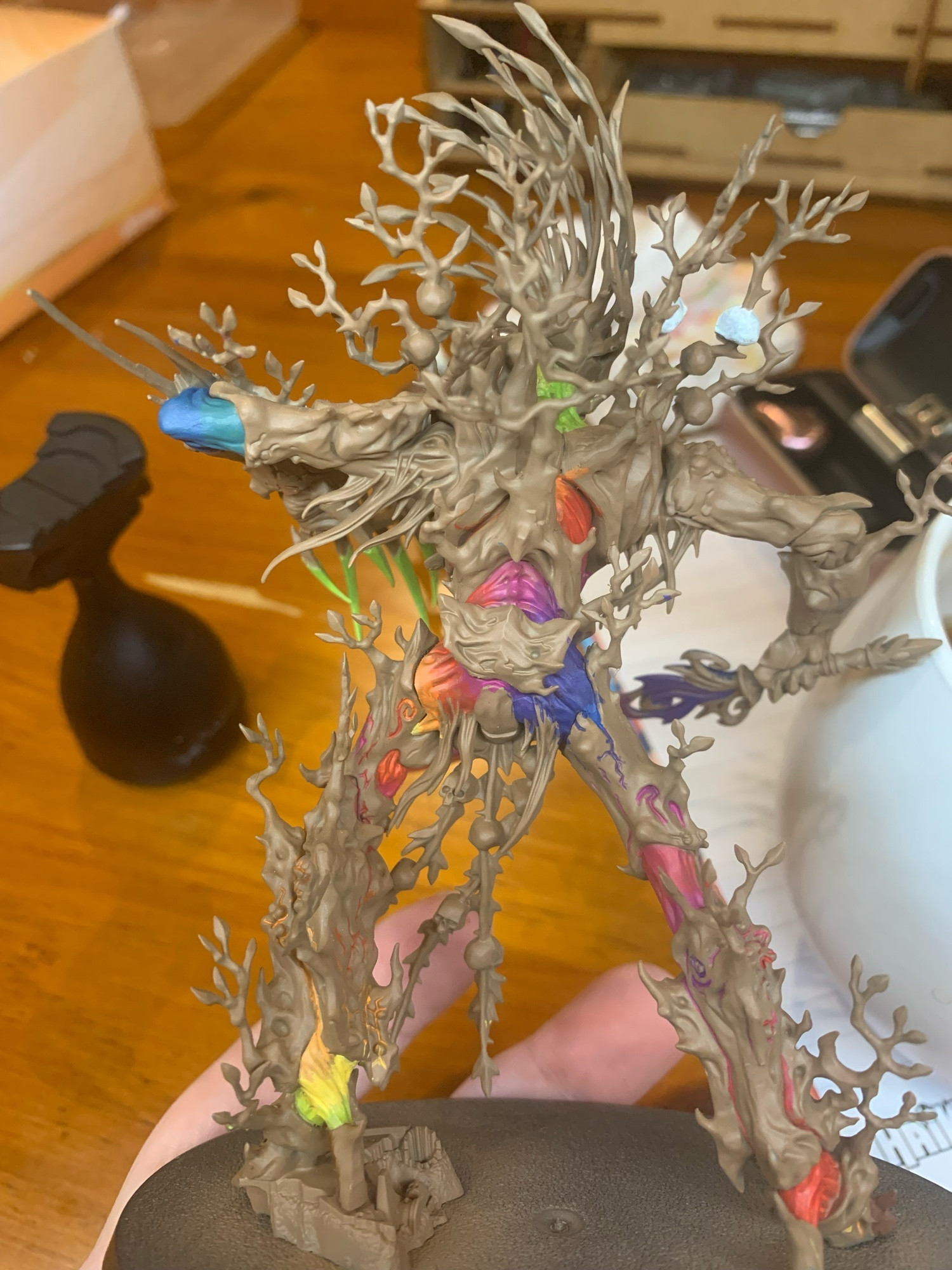 The back view of the humanoid tree mini holding a big sword. The mini has been undercoated brown and is being painted rainbow