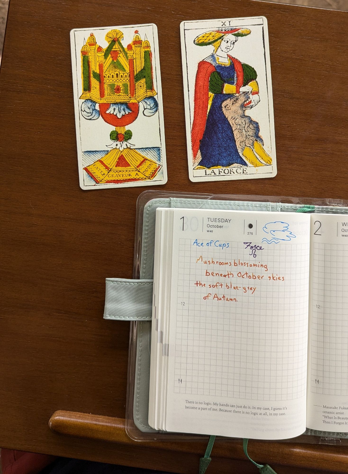 Photo of a day planner open to October 1 as well as two tarot cards. The cards are the Ace of Cups and the Force card from the Madenie. 

The day planner records those cards as well as the weather: cloudy. It has a poem:

"Mushrooms blossoming 
beneath October skies
the soft blue-grey
of Autumn."