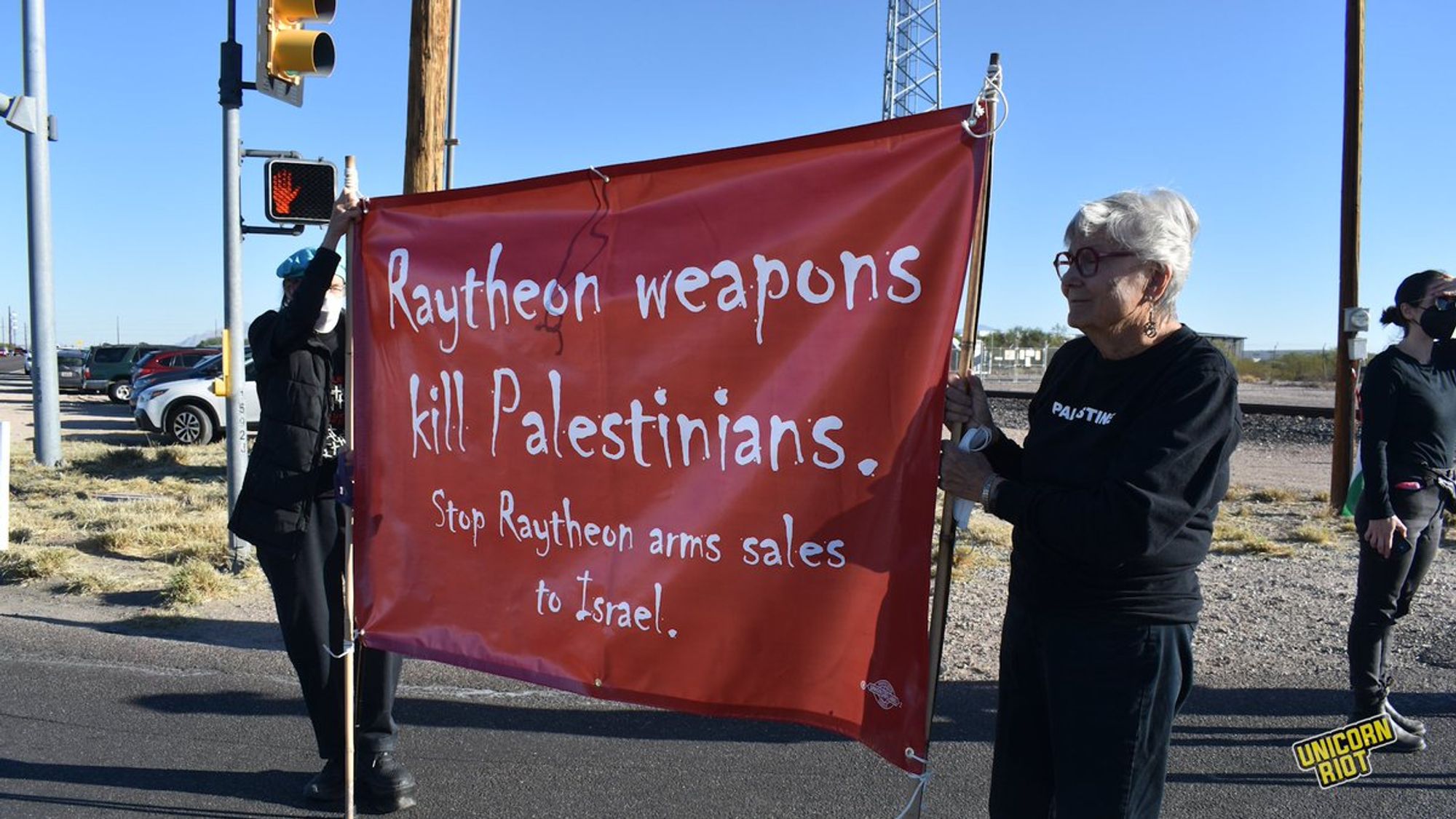 Lois Mastrangelo holds a banner reading “Raytheon weapons kill Palestinians: Stop Raytheon arms sales to Israel" while standing in the intersection outside Raytheon in Tucson.