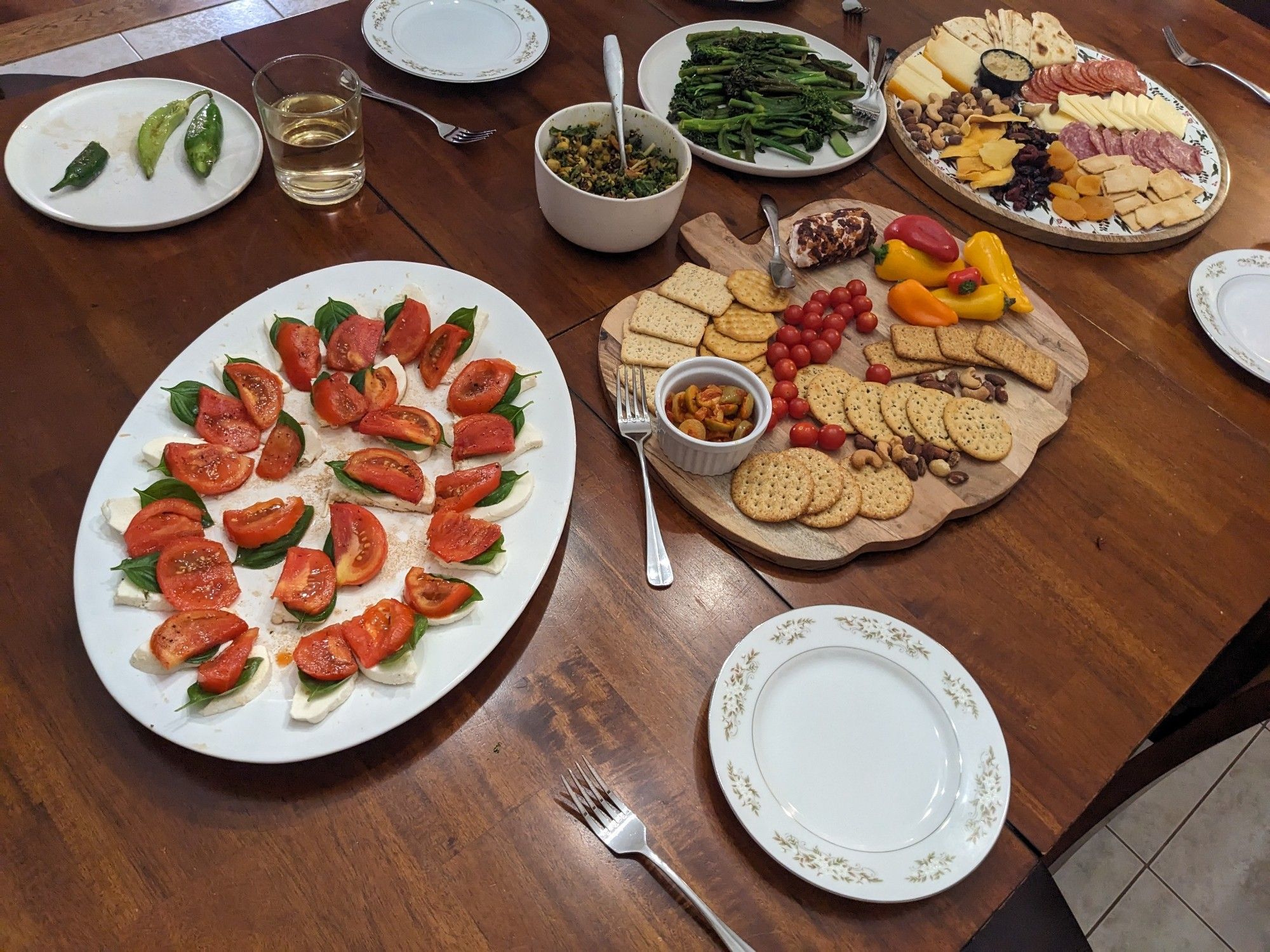 A dining table with several platters 

One platter of caprese salad
One platter of crackers, tomatoes, peppers, goat cheese and olives
One platter of meats, cheeses, nuts, dried fruits, pita, and hummus
A plate of roasted greens
A bowl of salad
My dad's plate of roasted hot peppers