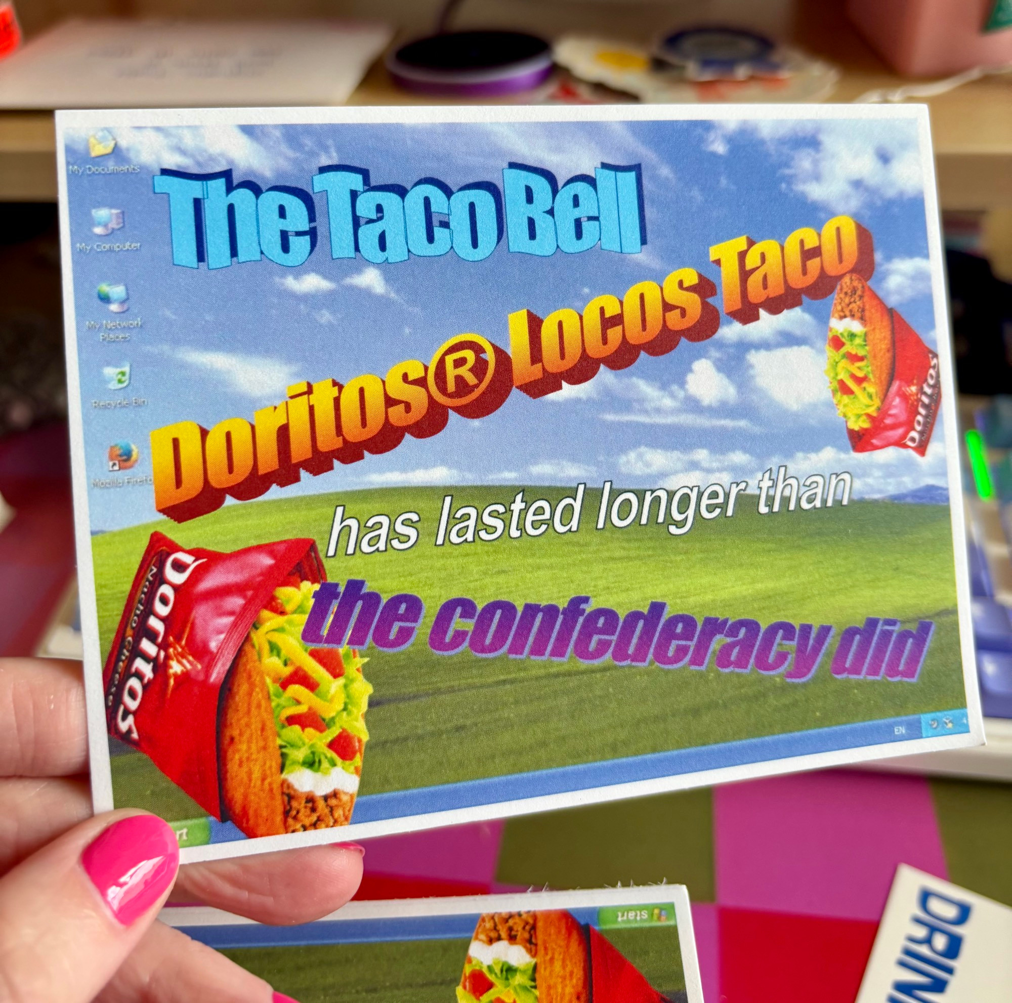 A postcard of the Windows 98 desktop with retro 90s word art that reads “the Taco Bell Doritos locos taco has lasted longer than the confederacy did”
