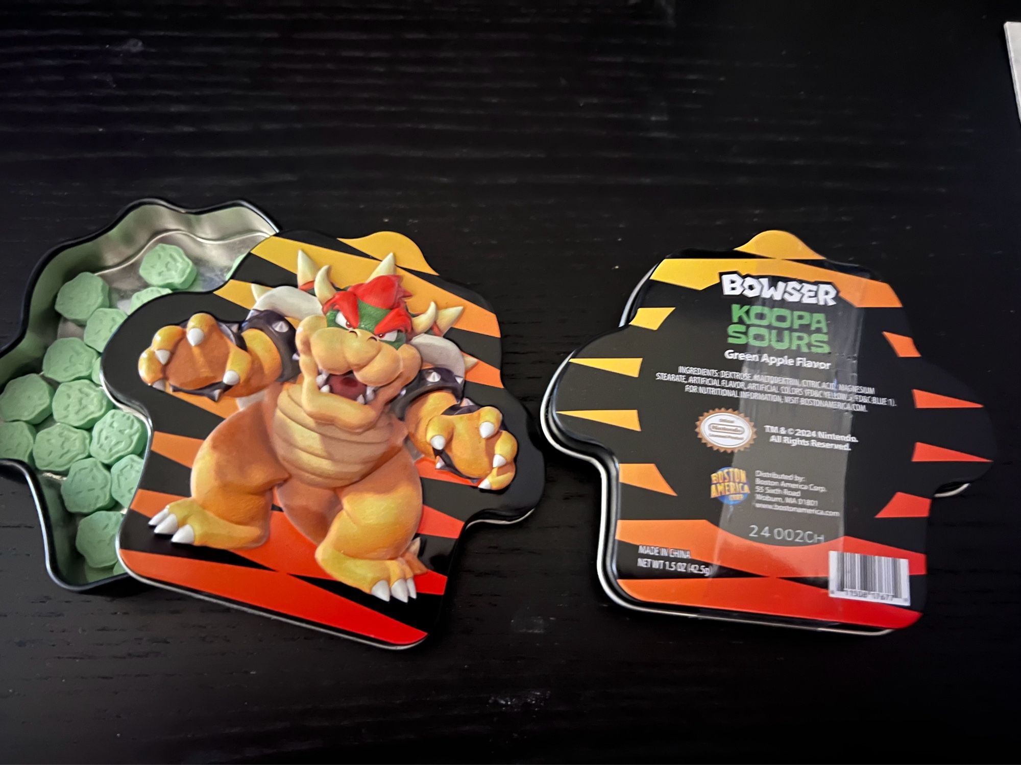 A tin of Bowser “koopa sours” candy, showing the front and back and the candy pieces