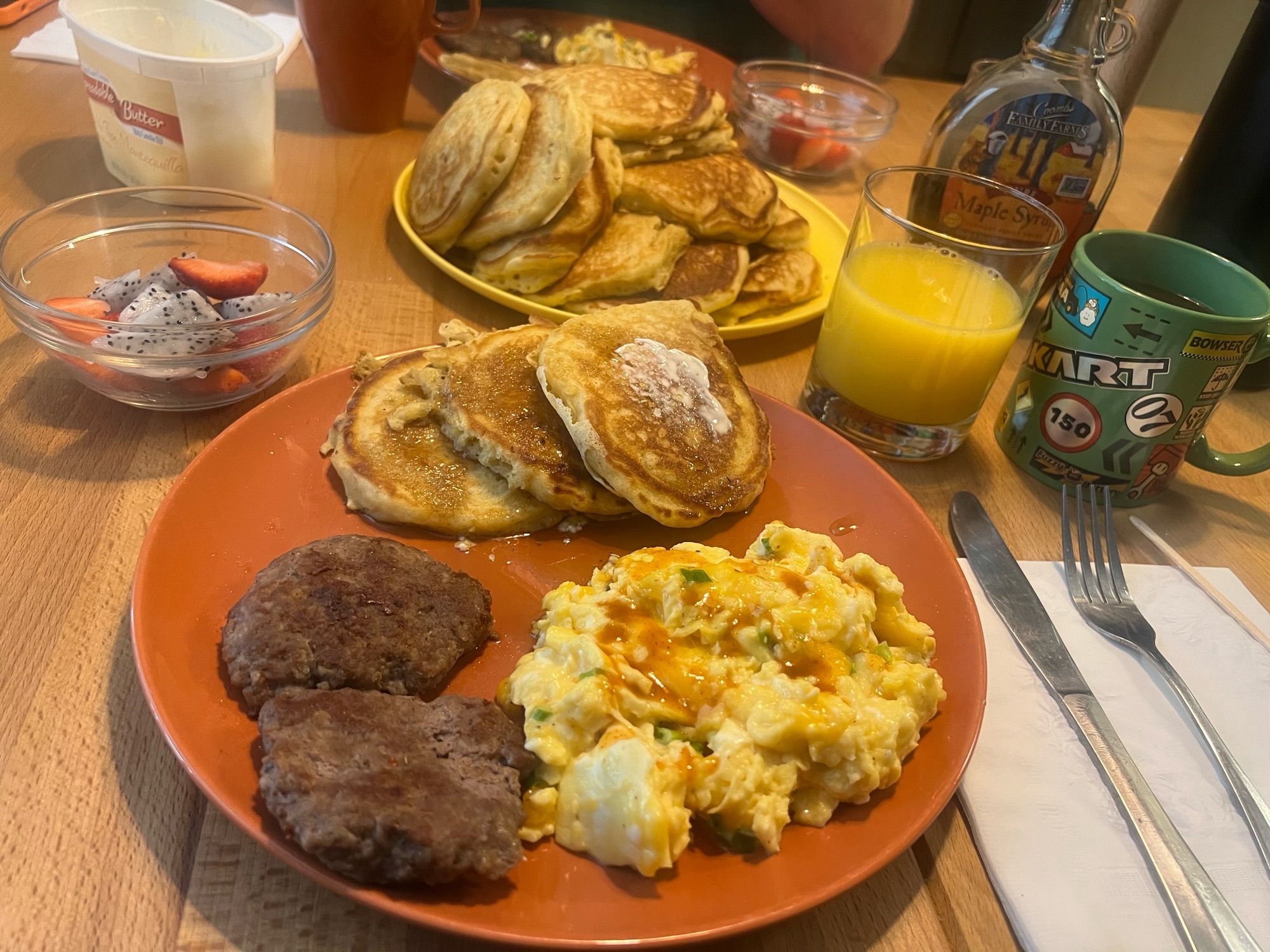 A full spread of the breakfast including eggs, sausage, a side dish of strawberries and dragonfruit, OJ, coffee, and of course pancakes