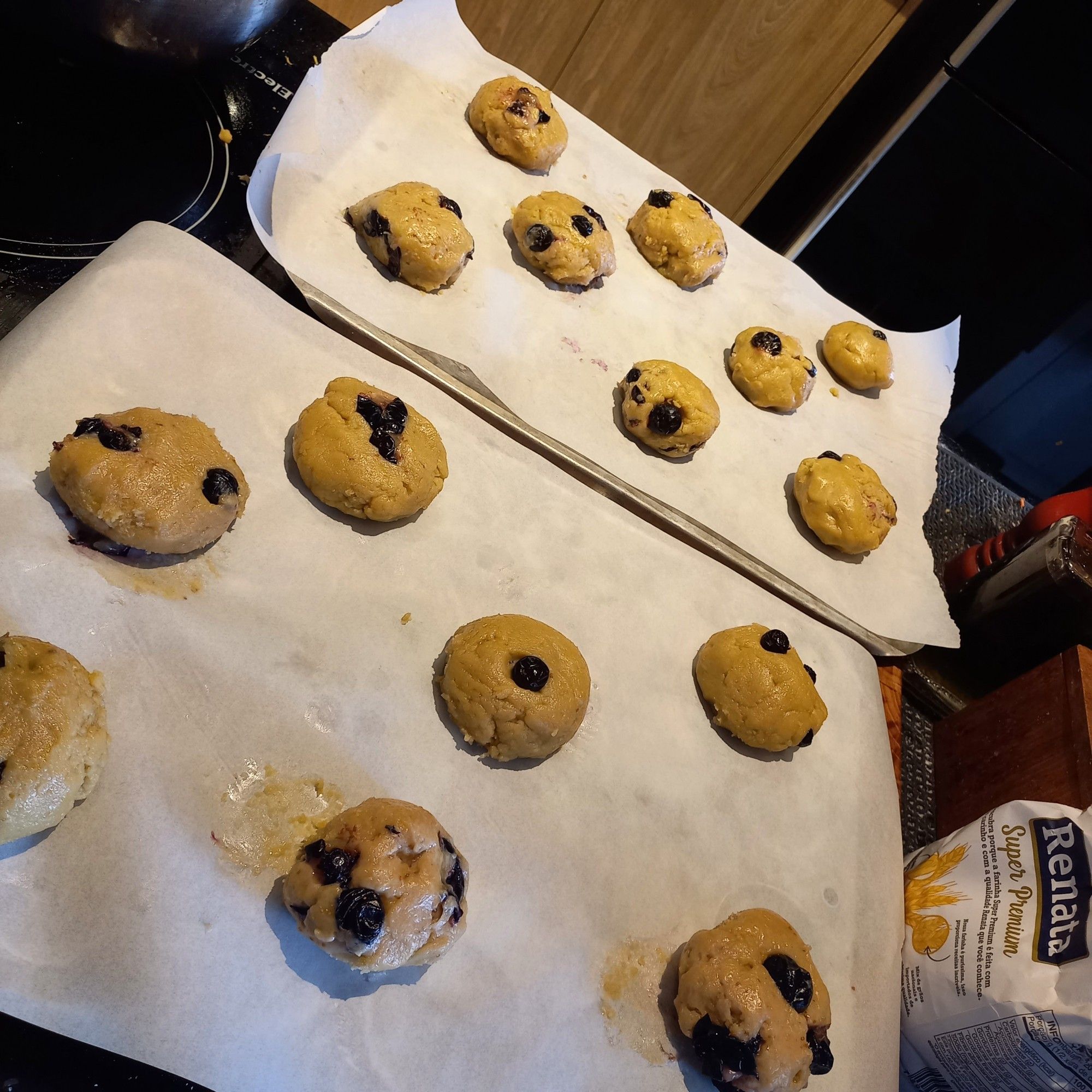 Duas folhas de papel manteiga com pequenos pedaços de massa de cookie com mirtilo antes de serem assadas.