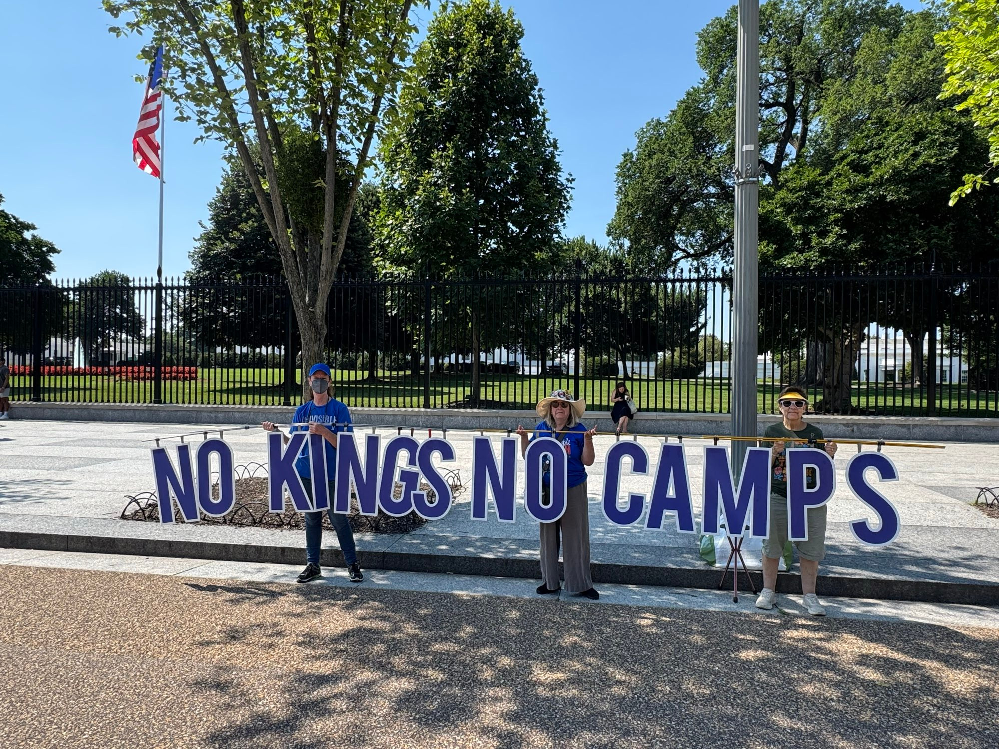 Activists hold sign NO KINGS NO CAMPS at White House