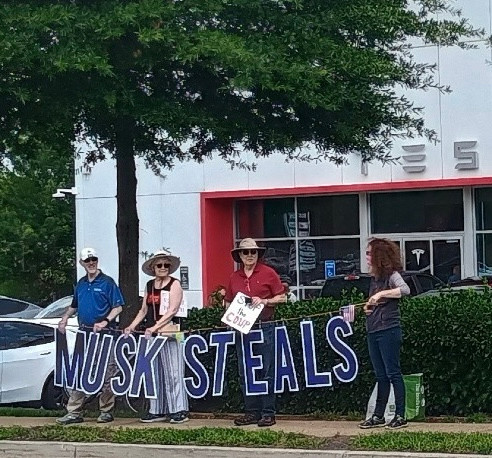 Activists hold sign MUSK STEALS at Tesla 
